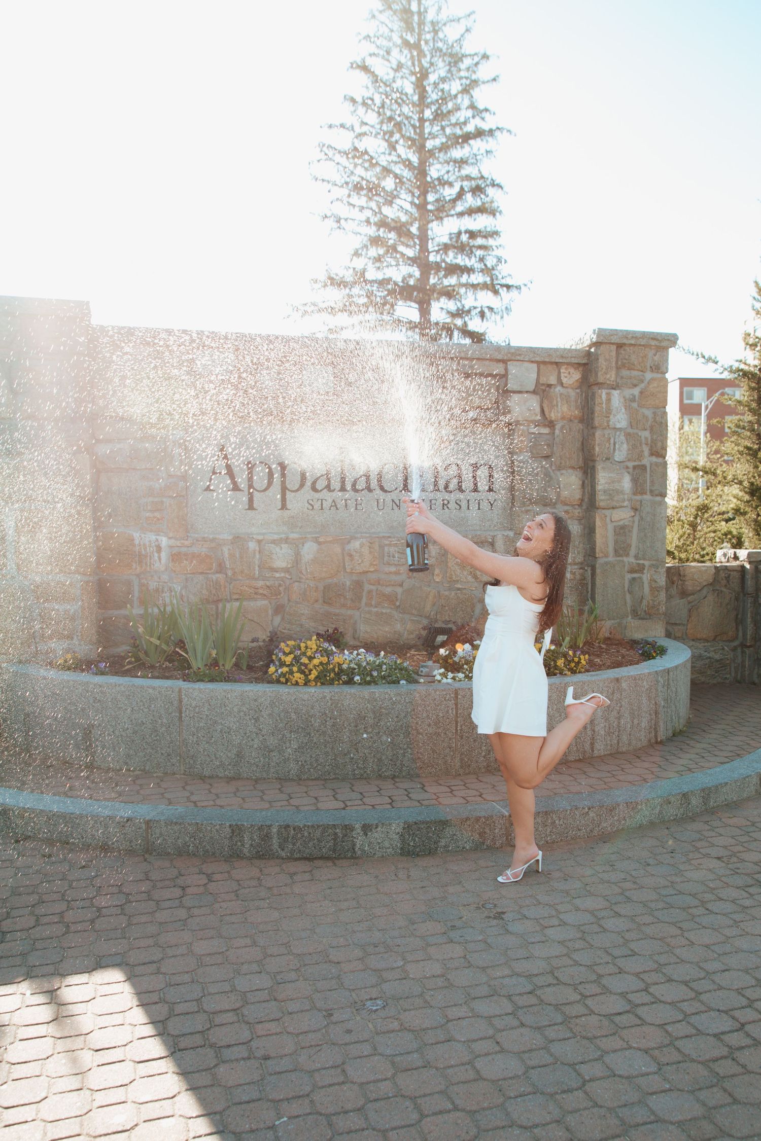 Celebrating graduate spraying champagne in front of Appalachian State University sign.