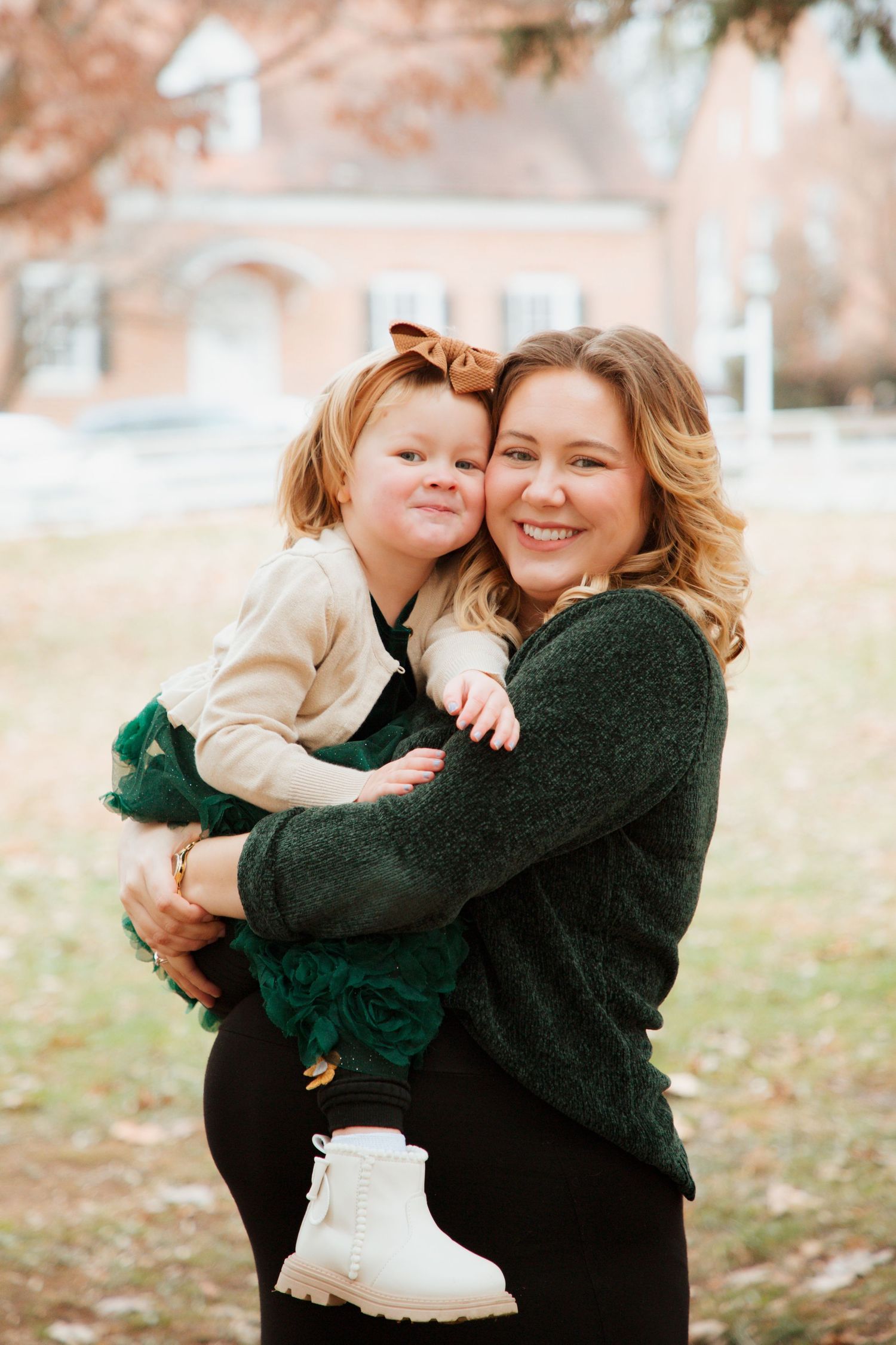 Smiling mother hugging toddler daughter in green dress during outdoor fall family photo session.