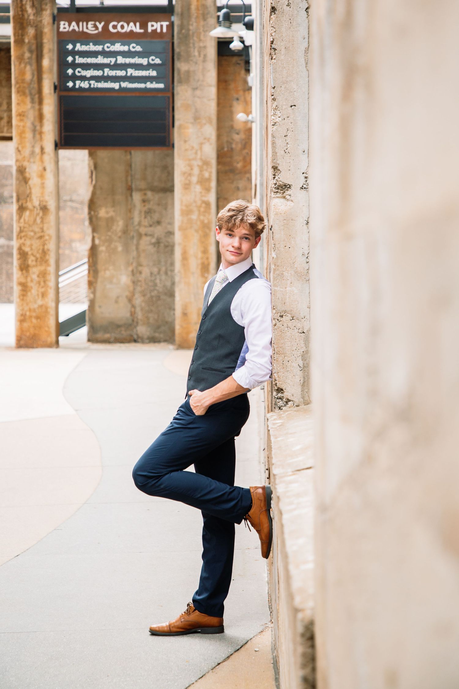 Stylish young man in vest and dress pants leaning against stone wall at Bailey Coal Pit.