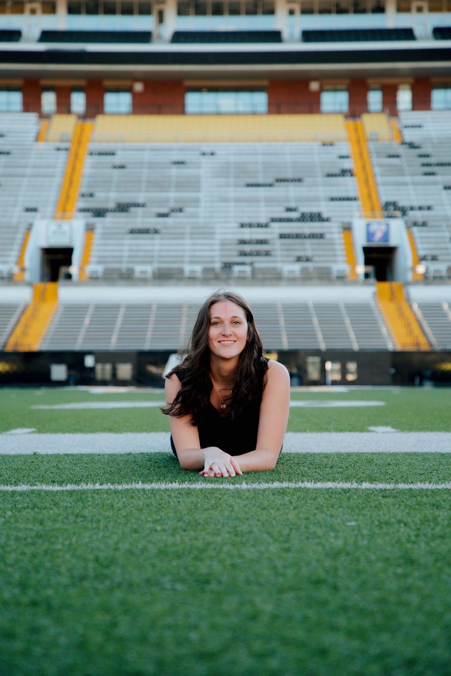 Smiling young woman in black dress lying on Appalachian State University football field turf.