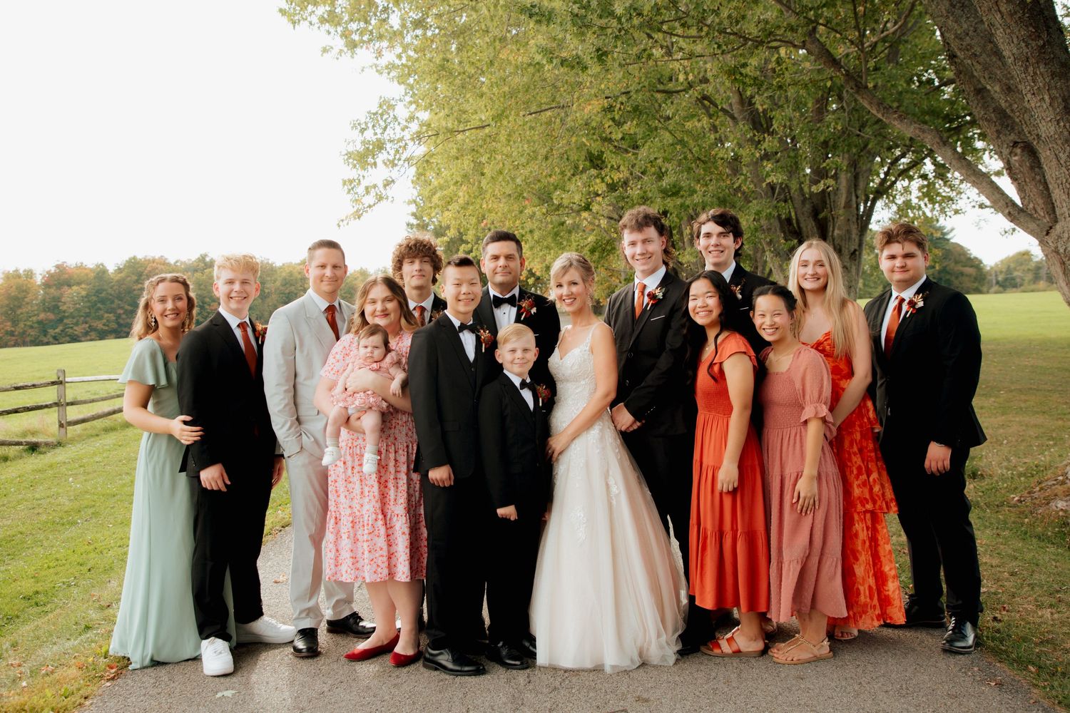Wedding party and family posing together on a tree-lined path in fall.