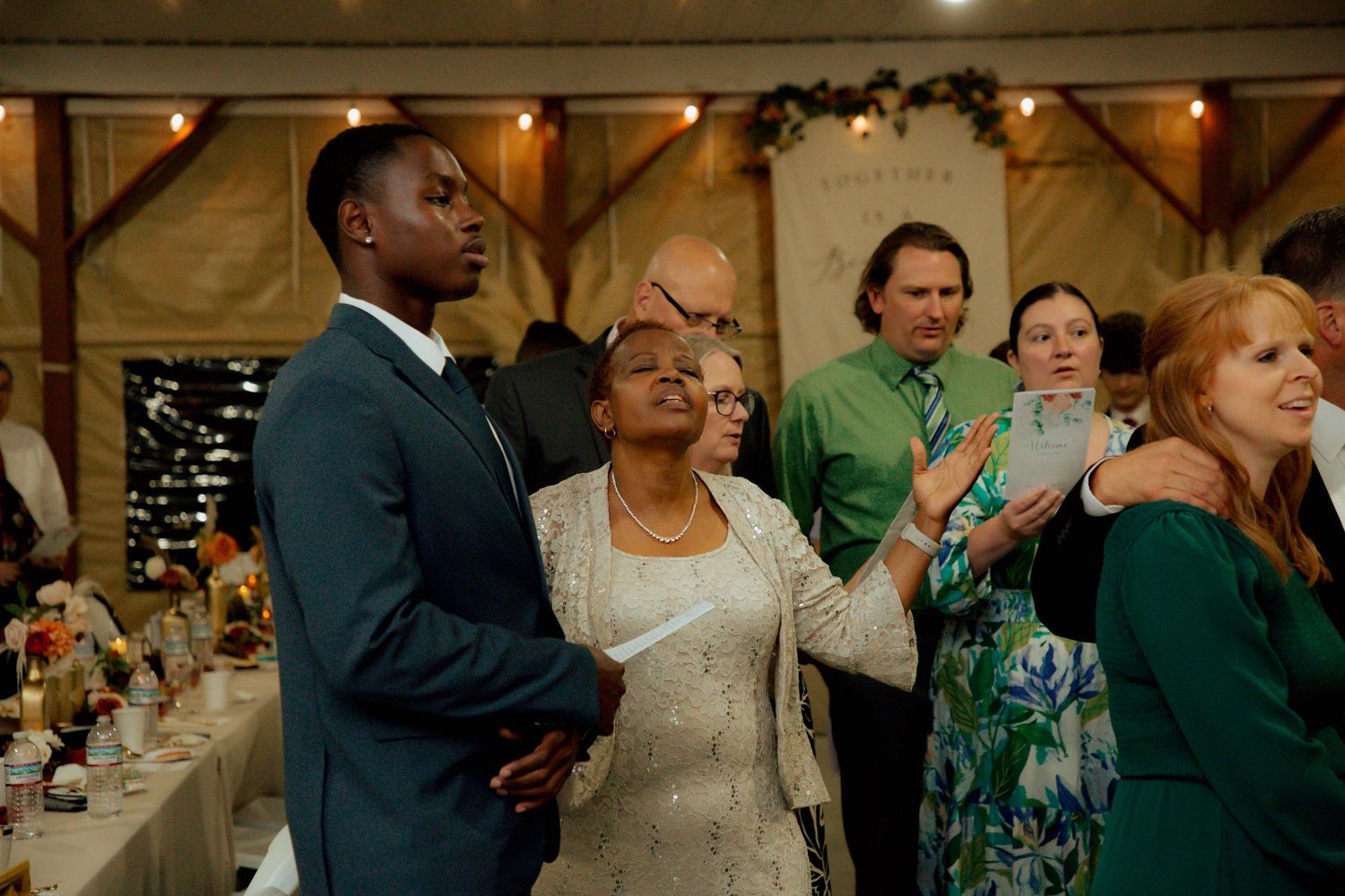 Diverse wedding guests gather attentively during a reception ceremony in a rustic barn venue.
