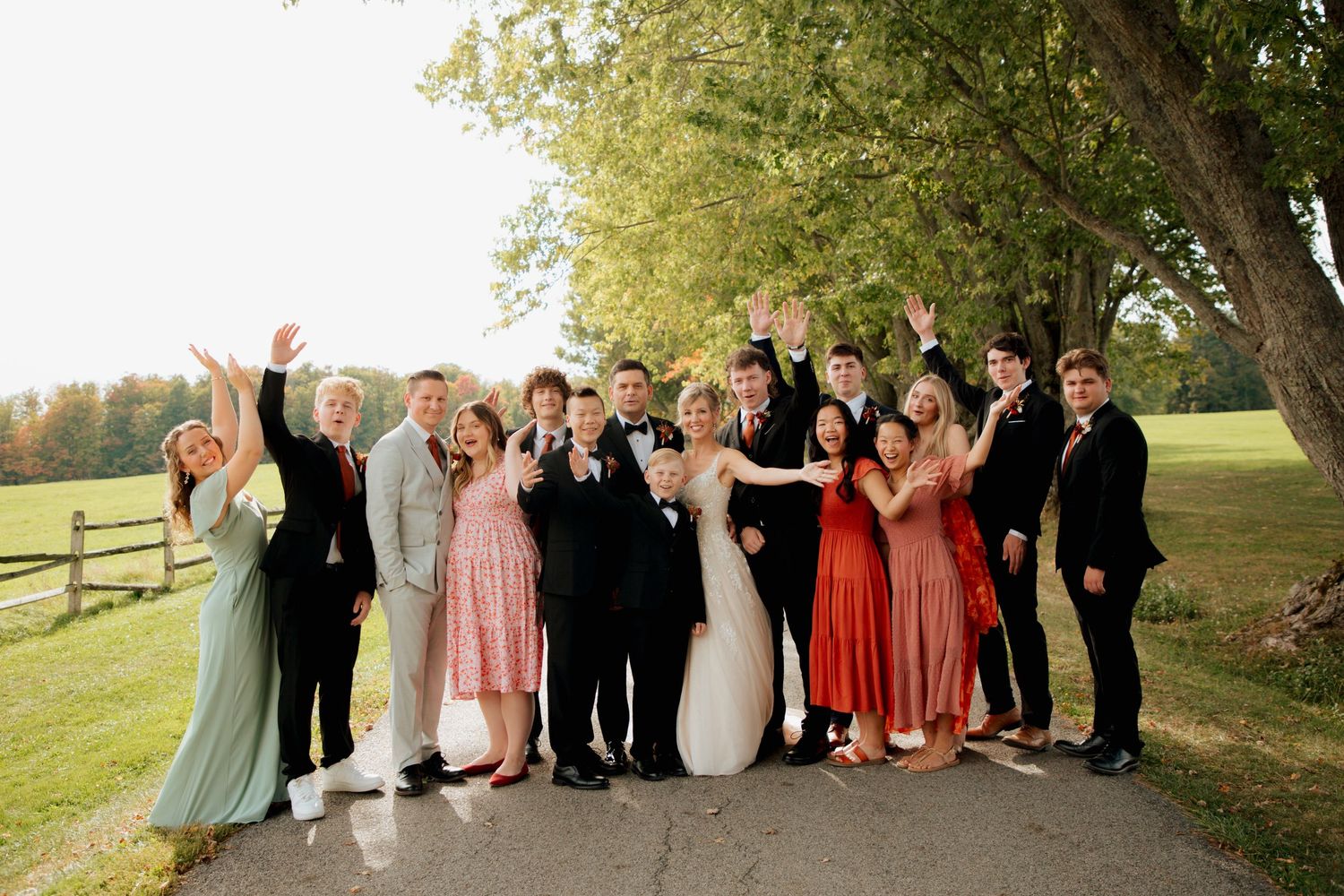 Large wedding party celebrating outdoors on a tree-lined path in autumn.
