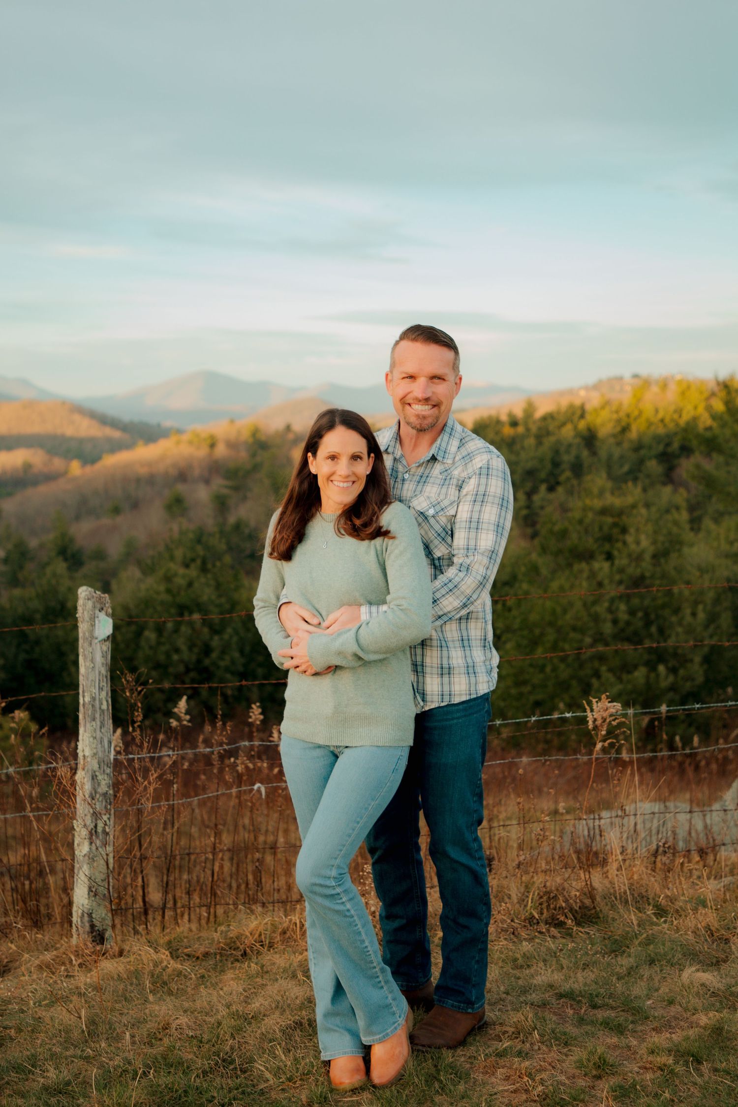 Couple embraces warmly while standing in front of a stunning mountain valley at golden hour.