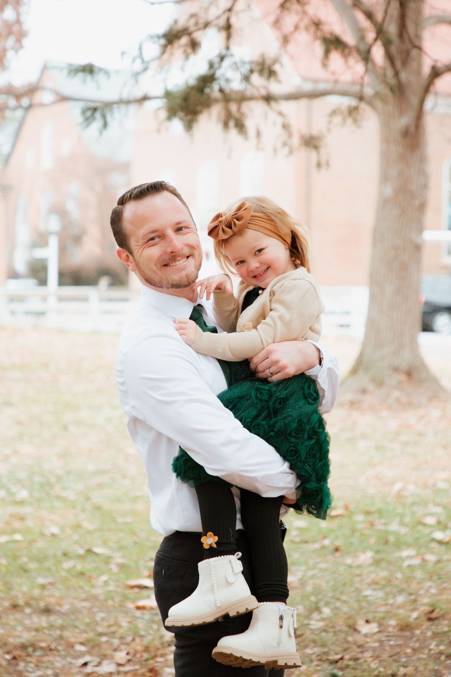 Father and toddler daughter in green dress smiling together during outdoor fall family portrait session.