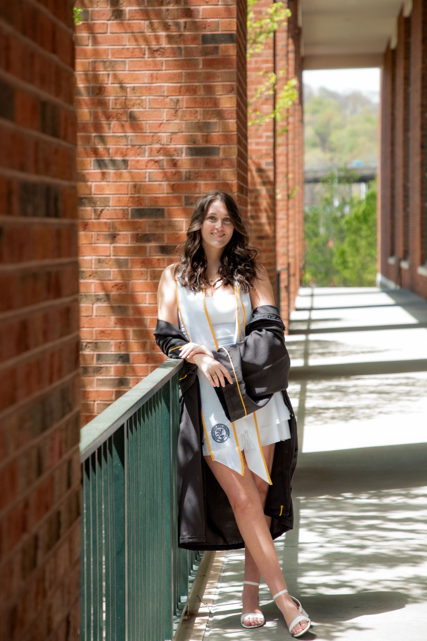 Smiling female graduate in black gown leaning on railing in brick hallway at Appalachian State University.