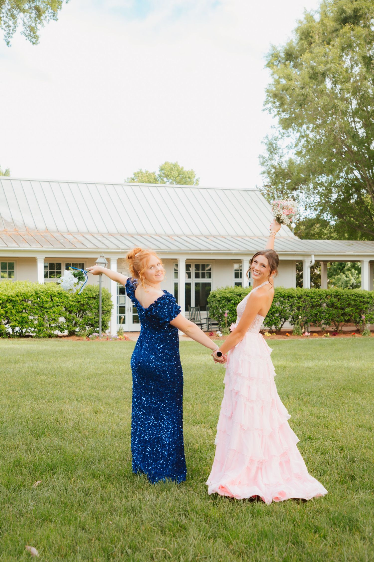 Two women in formal gowns dancing outdoors, one in navy sequin dress and one in pink ruffle gown with bouquet.