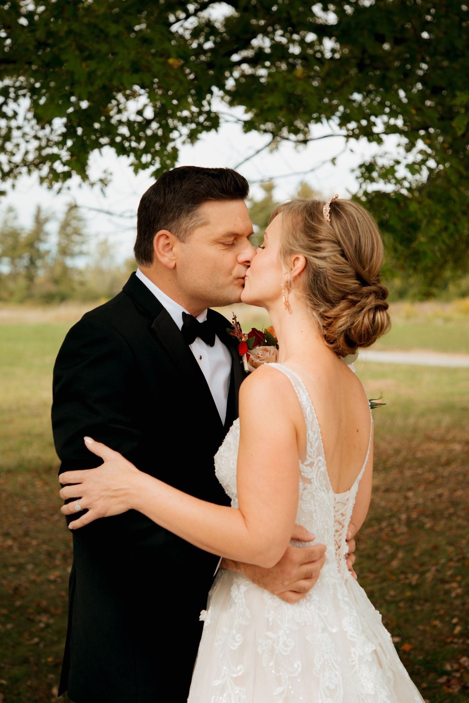 Bride and groom sharing romantic first kiss under autumn trees at outdoor wedding.
