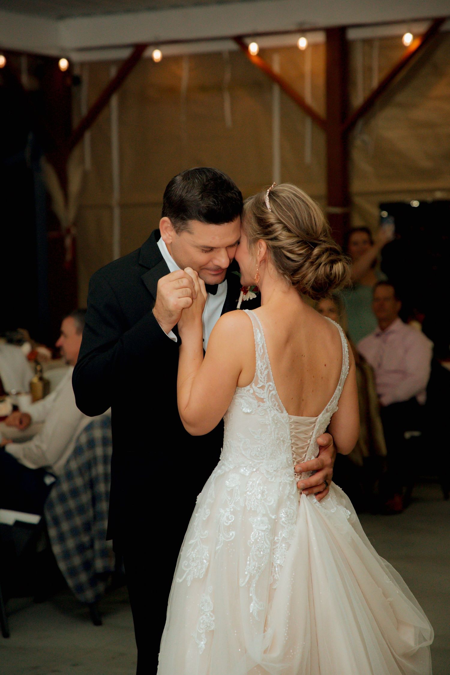 Bride and groom share an emotional first dance in a warmly lit barn wedding reception venue.