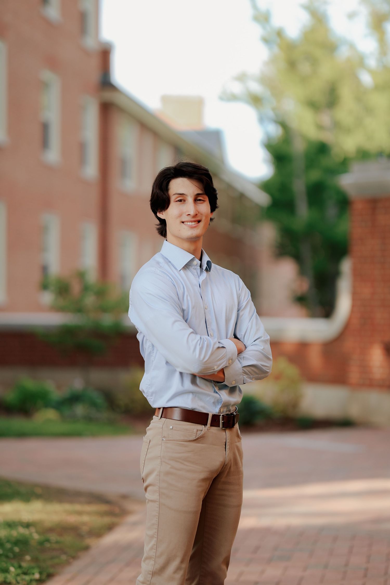 Smiling young man with crossed arms posing in front of a brick university building.