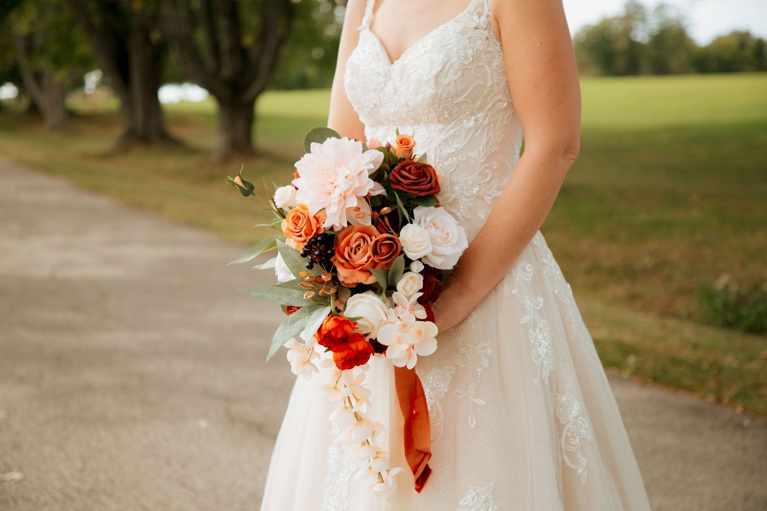 Close-up of a bridal bouquet featuring burnt orange, red, and white roses with a satin ribbon accent.