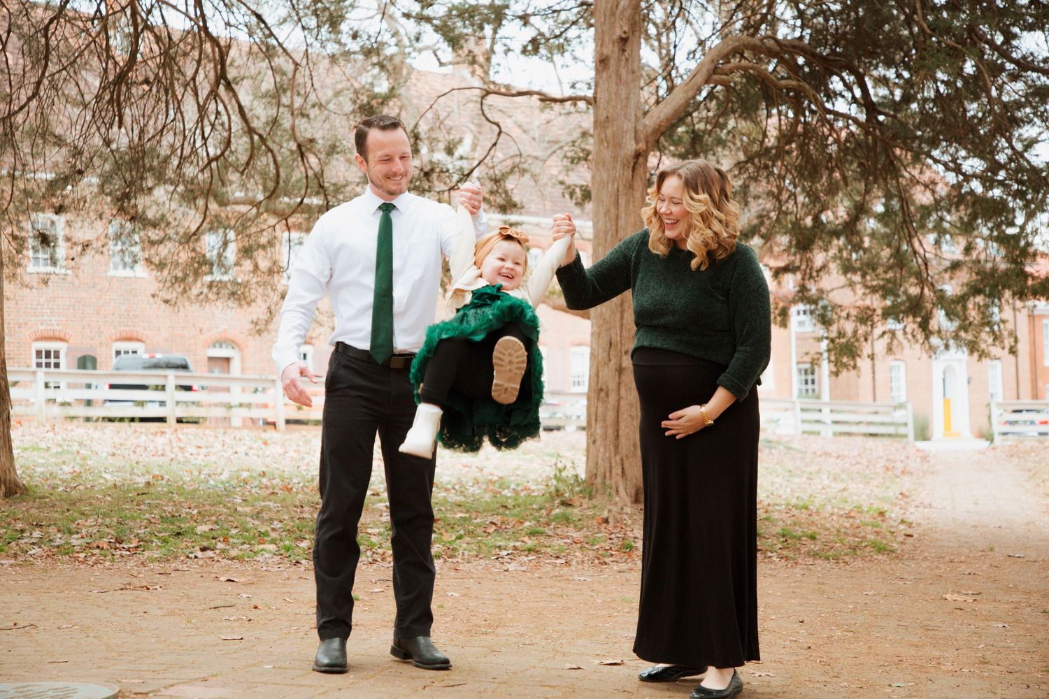 Pregnant woman and husband swinging their toddler child by the hand outdoors in fall.