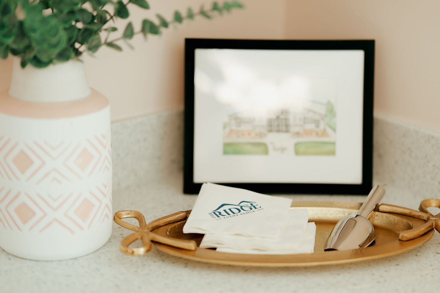 Gold tray with wedding stationery and pen beside white vase with eucalyptus on marble surface.