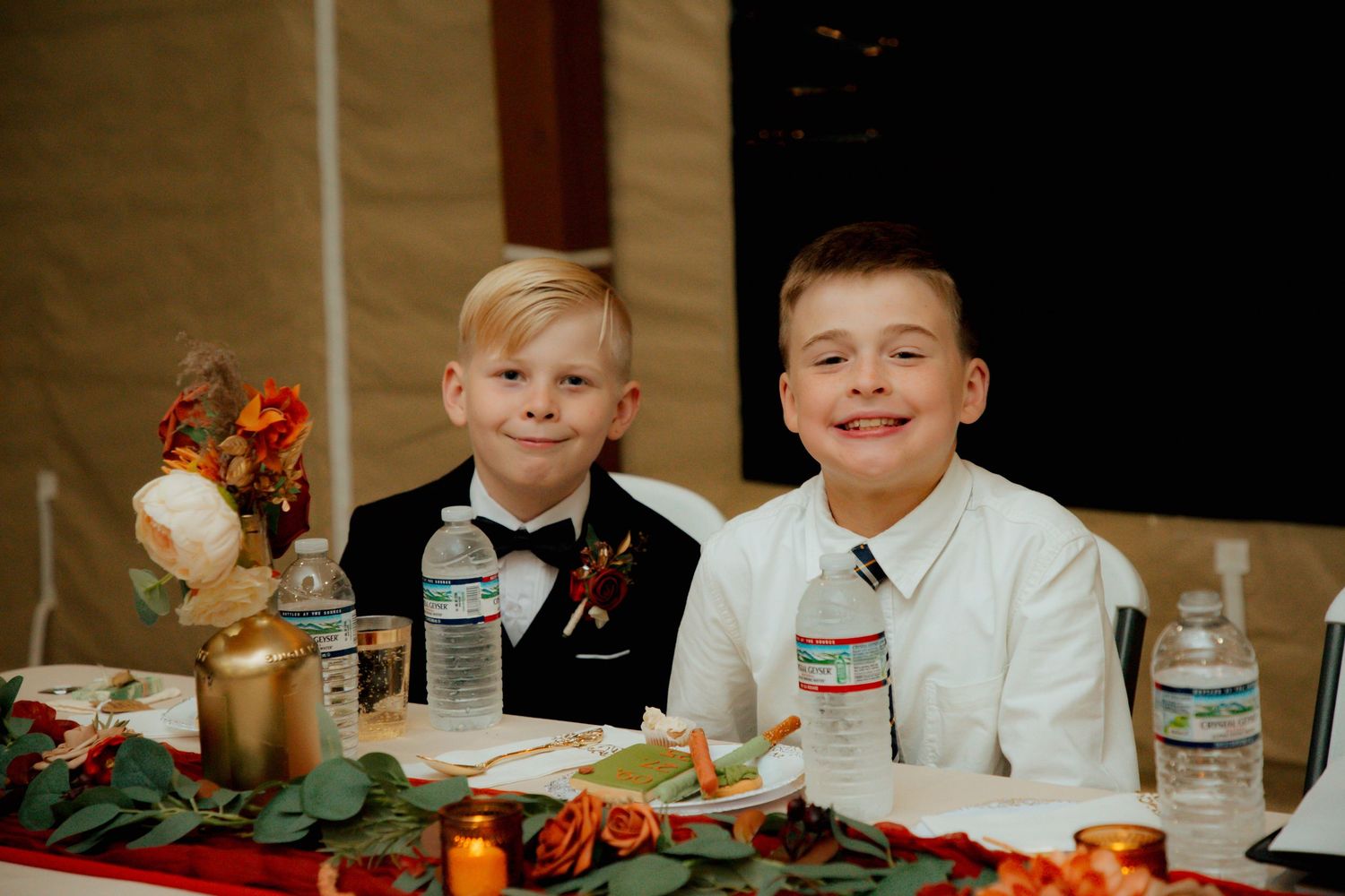 Two young boys smile at the wedding head table decorated with fall florals.