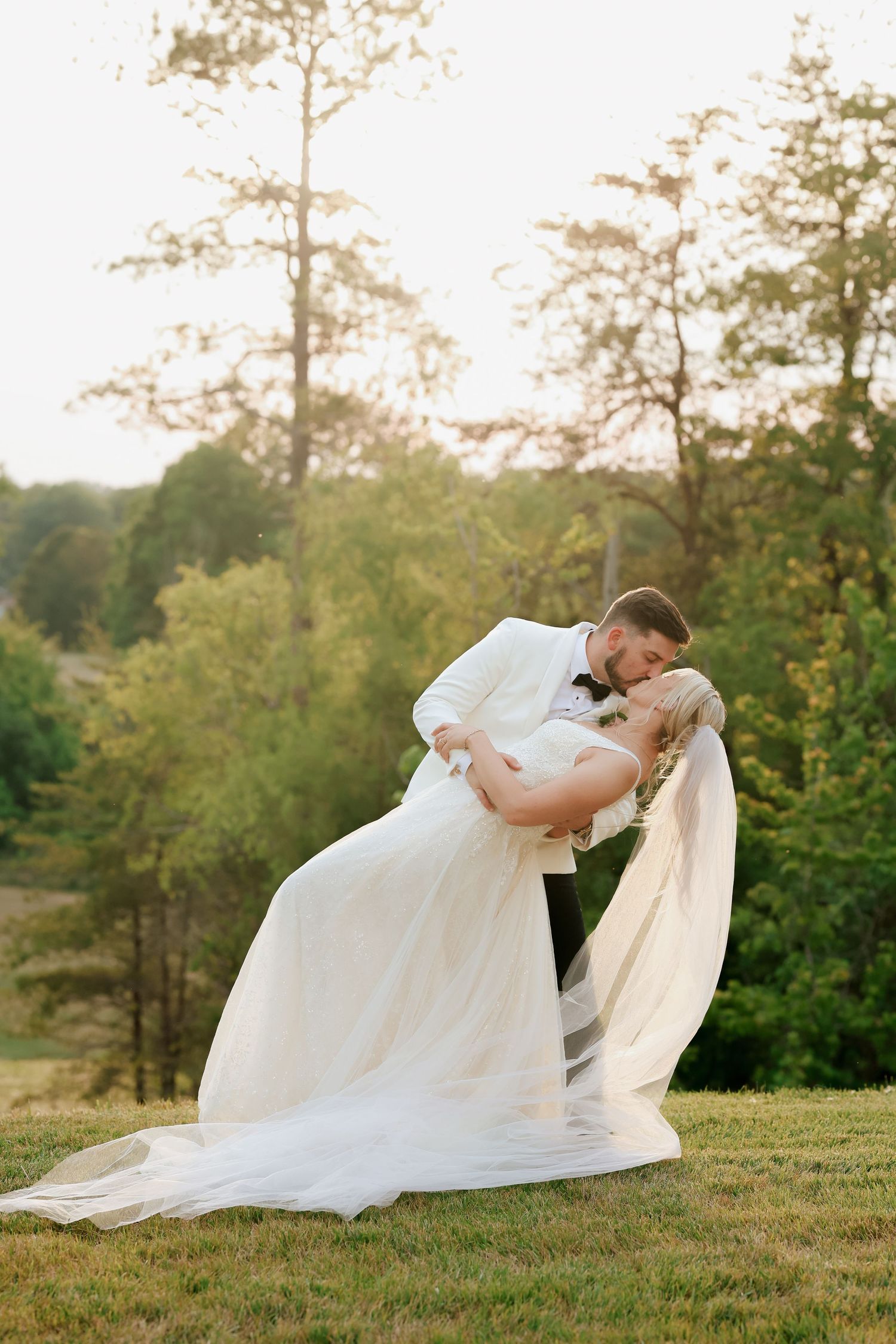 Groom dipping bride for a romantic kiss outdoors during golden hour wedding portrait session.