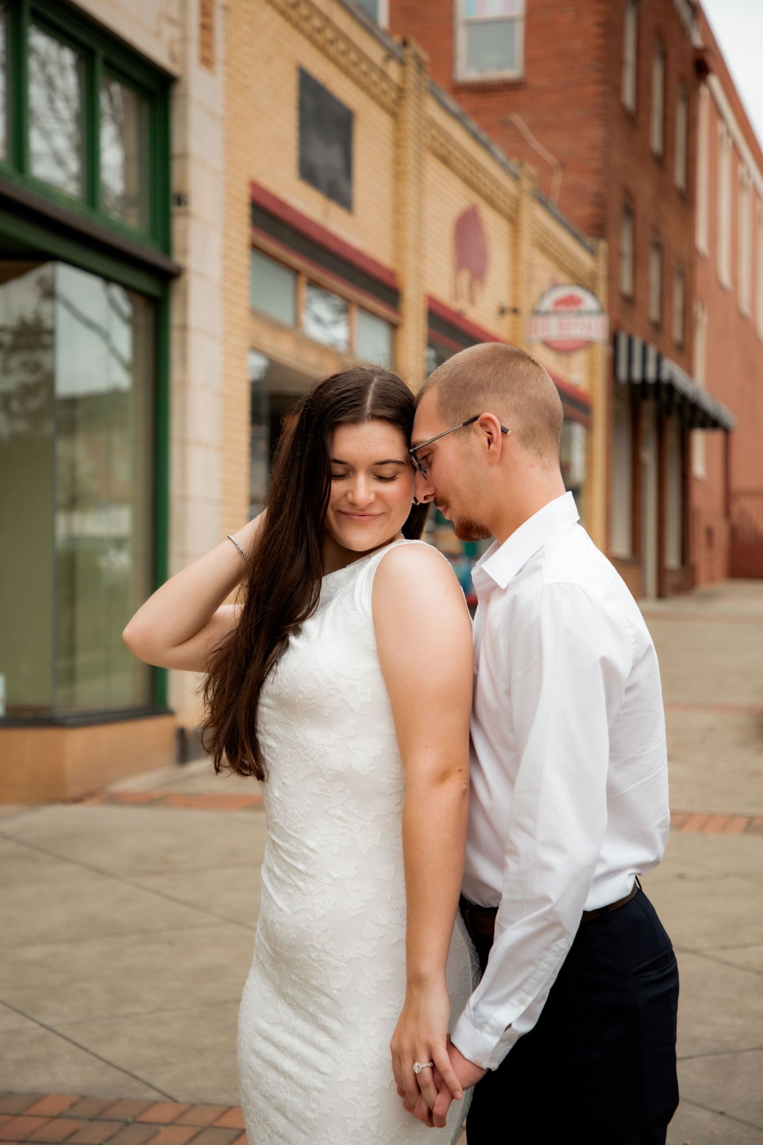 Bride in white dress and groom holding hands on a charming brick downtown street.