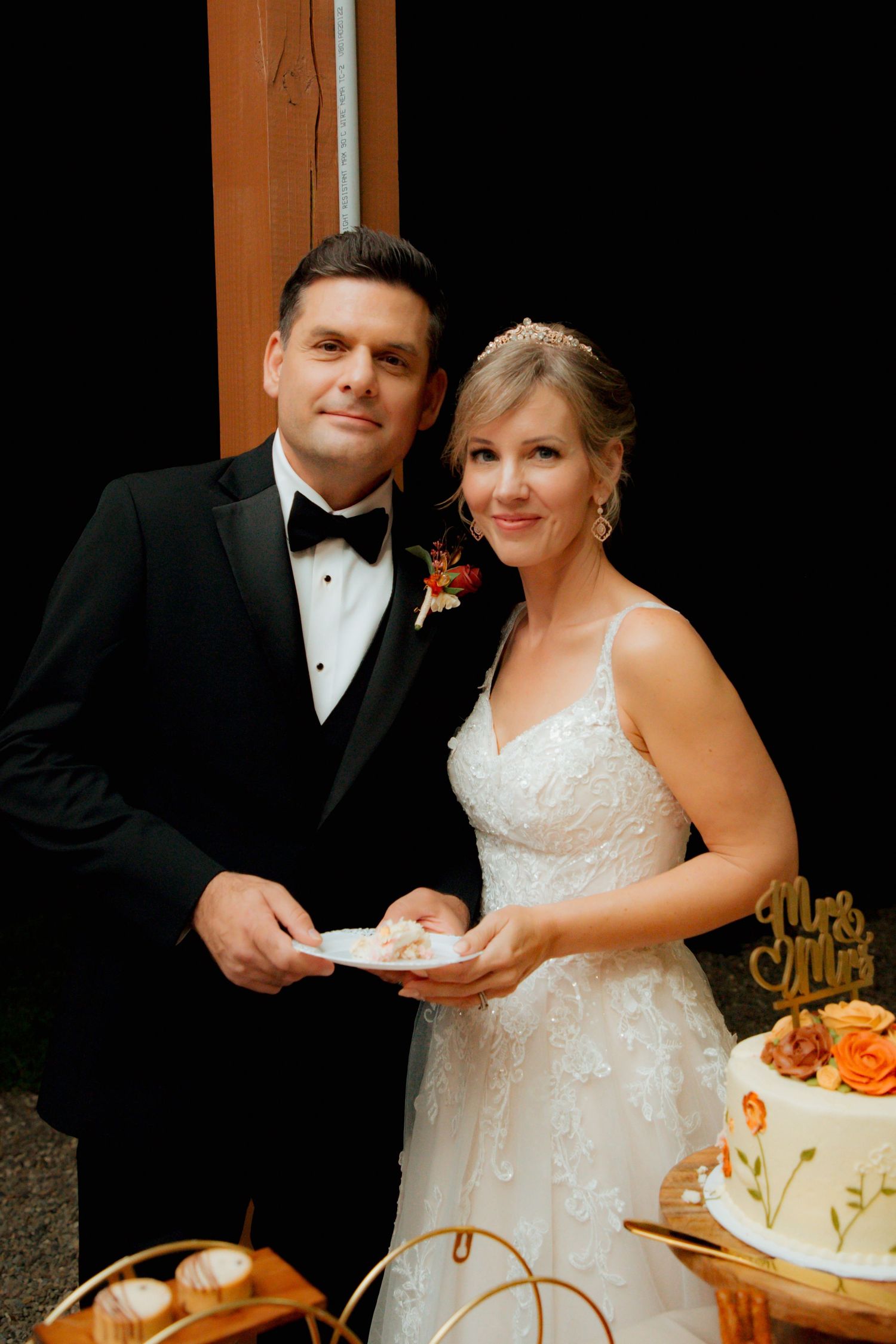 Smiling bride and groom pose together holding cake plates at their wedding reception.