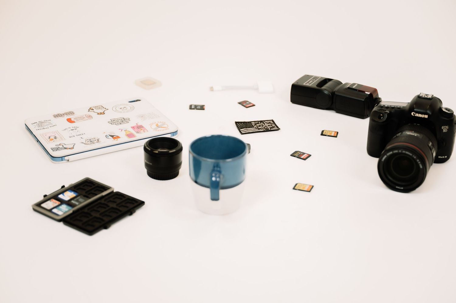 Flat lay of Canon DSLR camera, lenses, memory cards, and photography accessories on white surface.