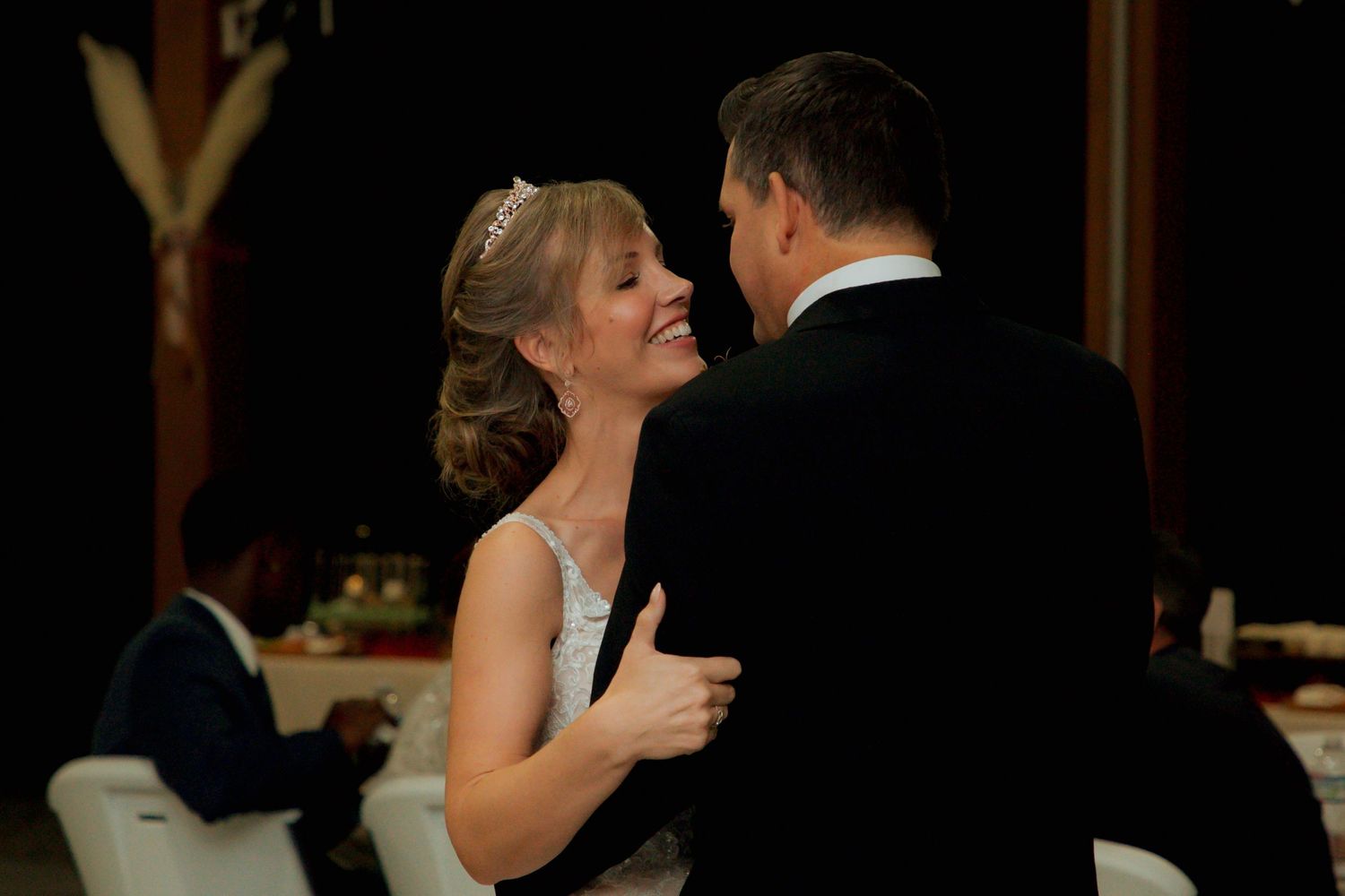 Radiant bride wearing tiara smiles at groom during their first dance at wedding reception.
