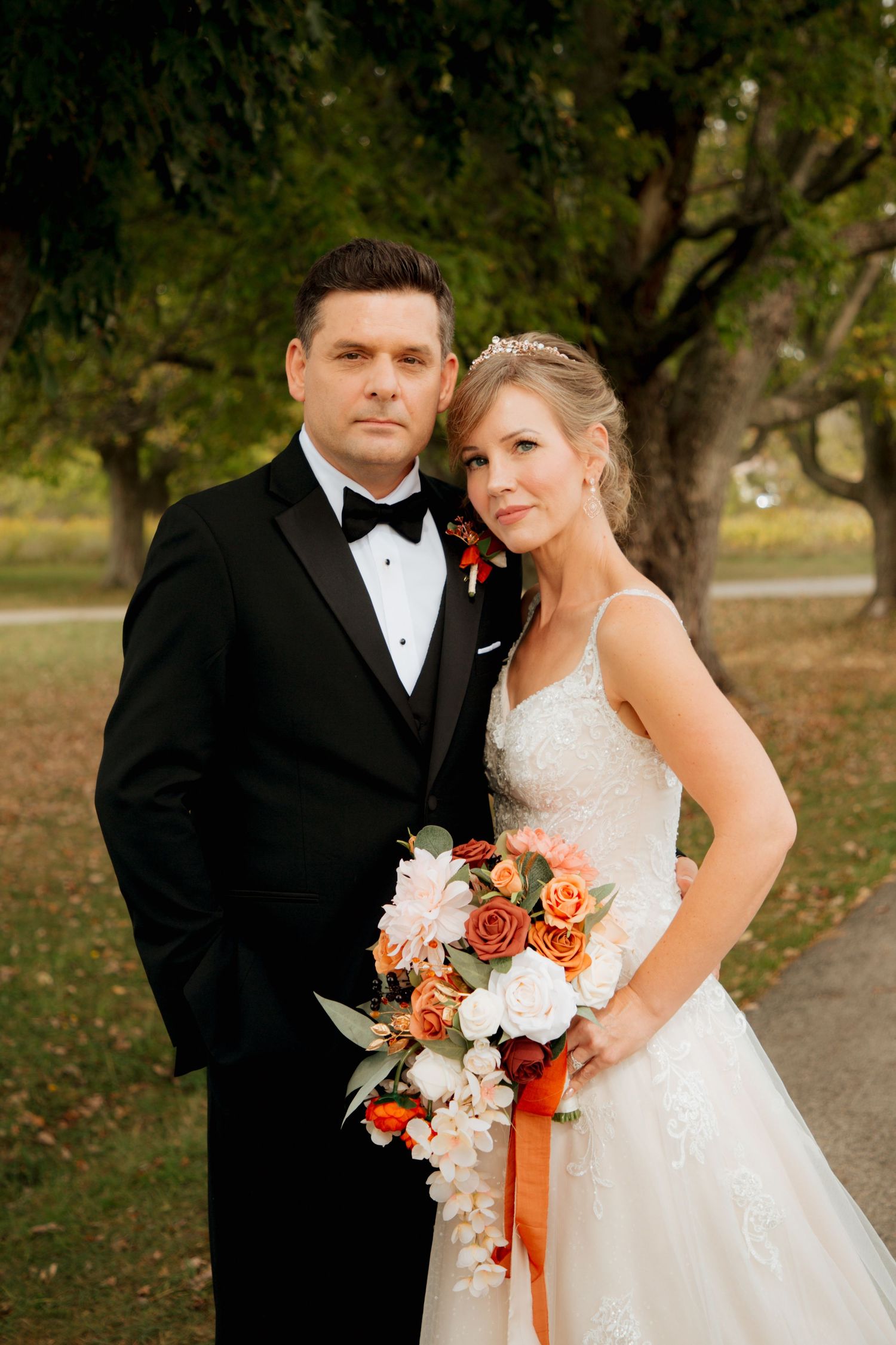 Bride and groom posing formally with cascading orange and white bouquet at fall wedding.
