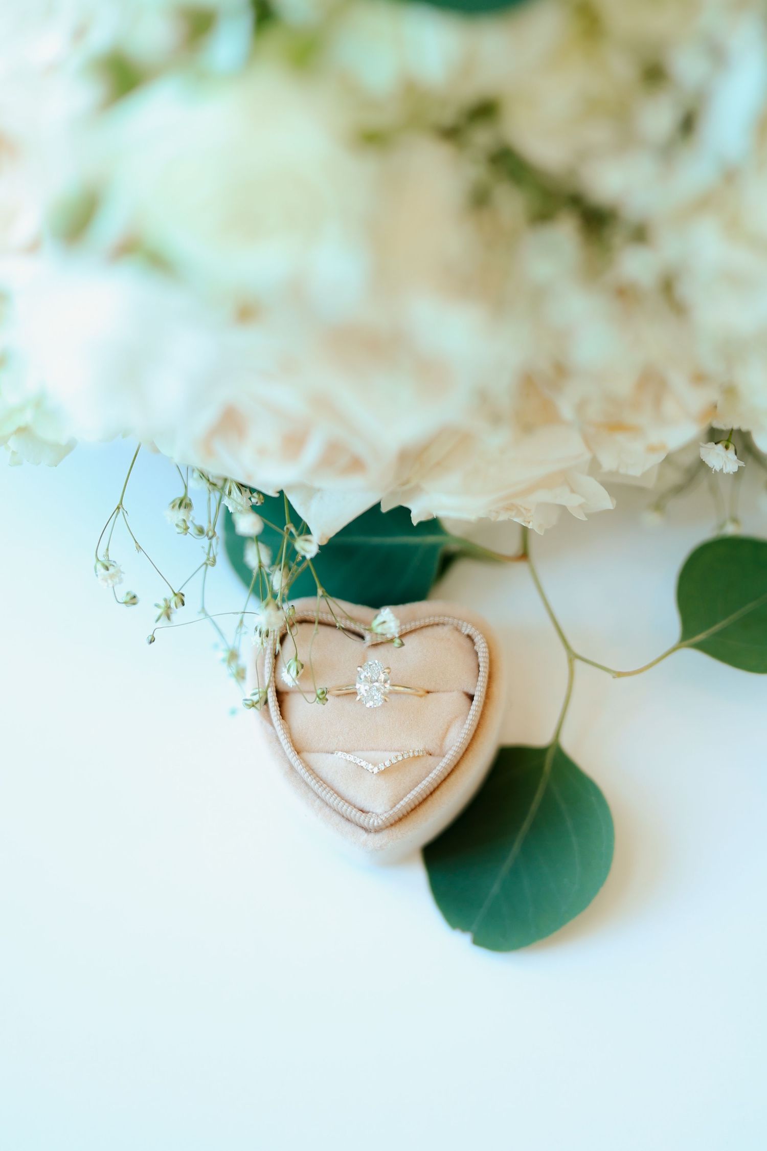 Diamond engagement ring in heart-shaped wooden ring box with white floral bouquet.