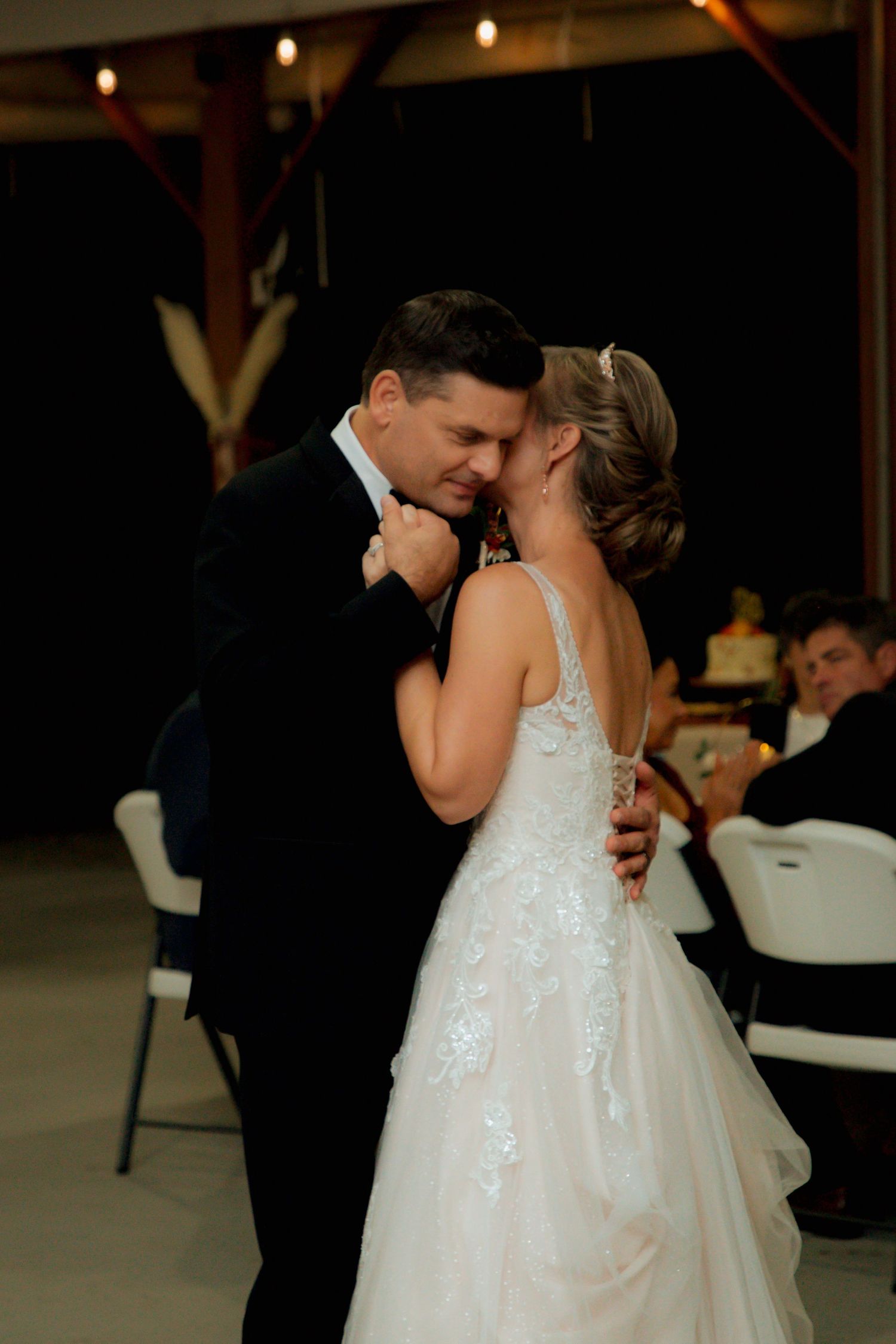 Bride and groom share an intimate first dance moment under string lights at barn wedding.