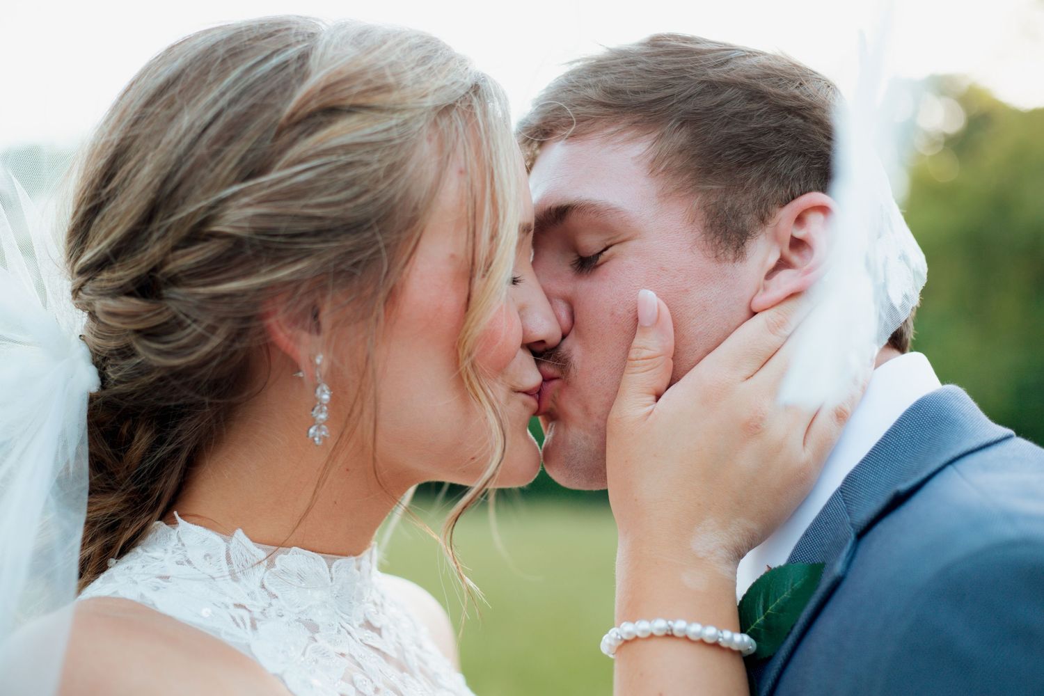 Bride and groom share a passionate kiss with bride holding grooms face tenderly.