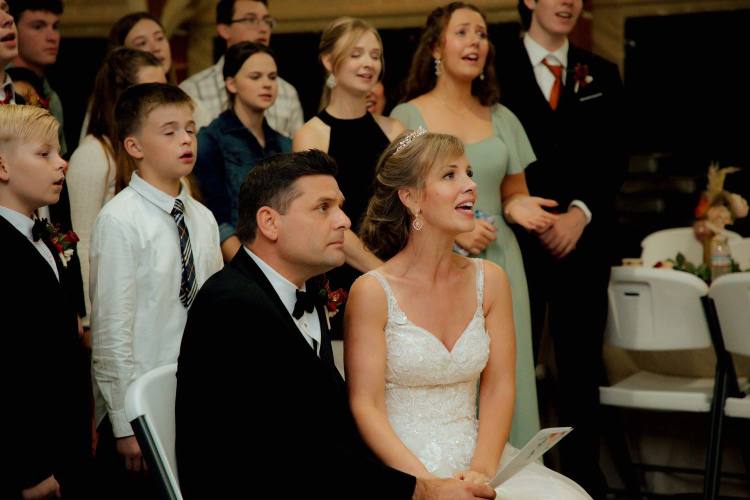 Bride in white lace gown and groom in tuxedo sit together during emotional wedding ceremony.