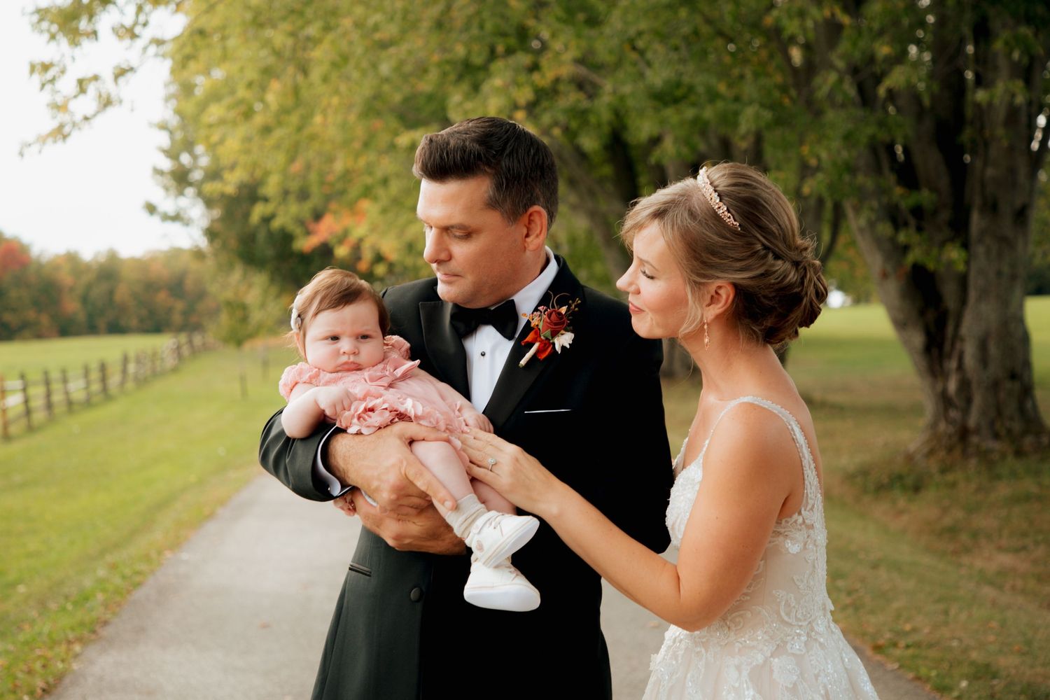 Bride and groom tenderly holding a baby girl outdoors at wedding.