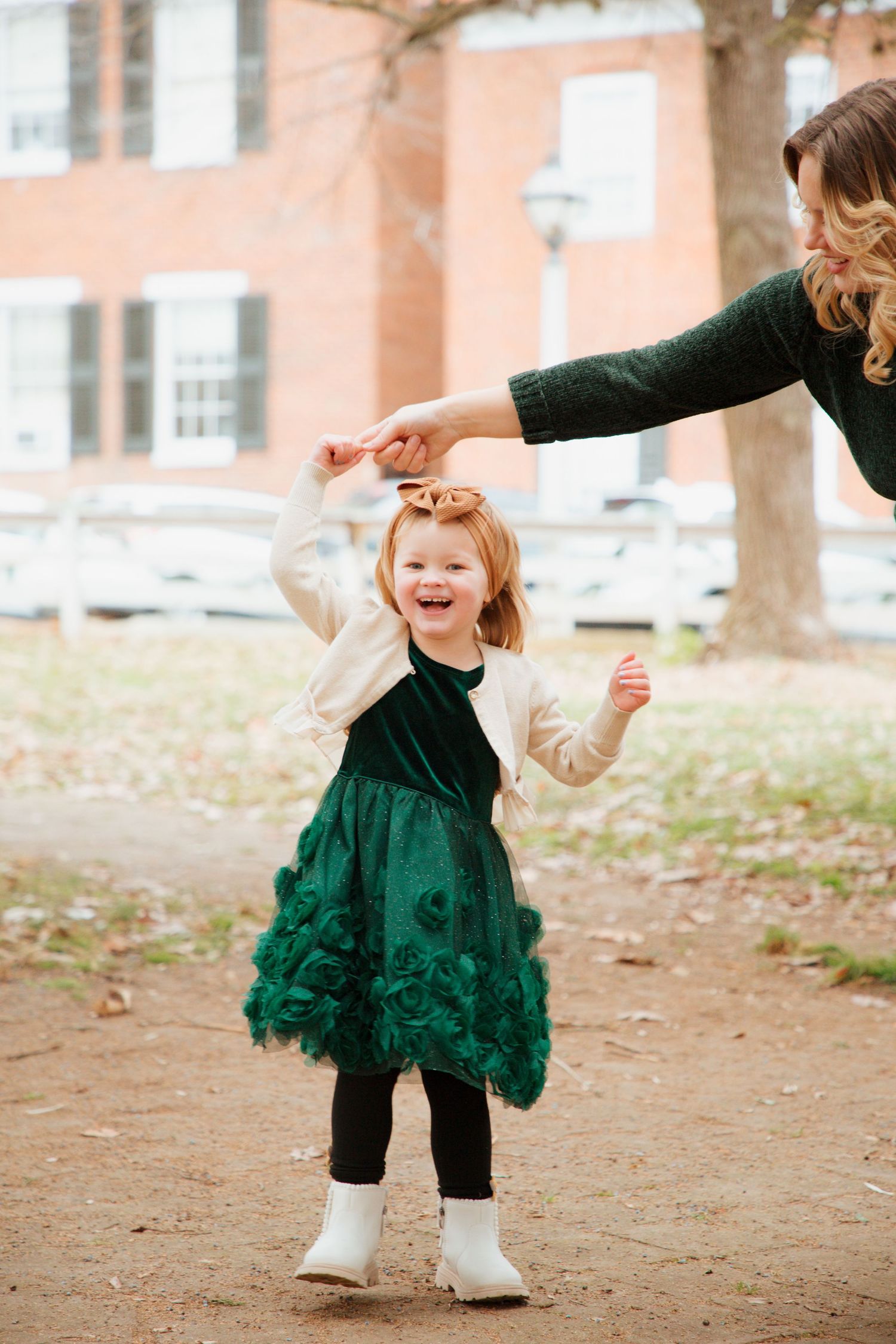 Joyful toddler girl in green dress spinning with mother during outdoor fall family photos.