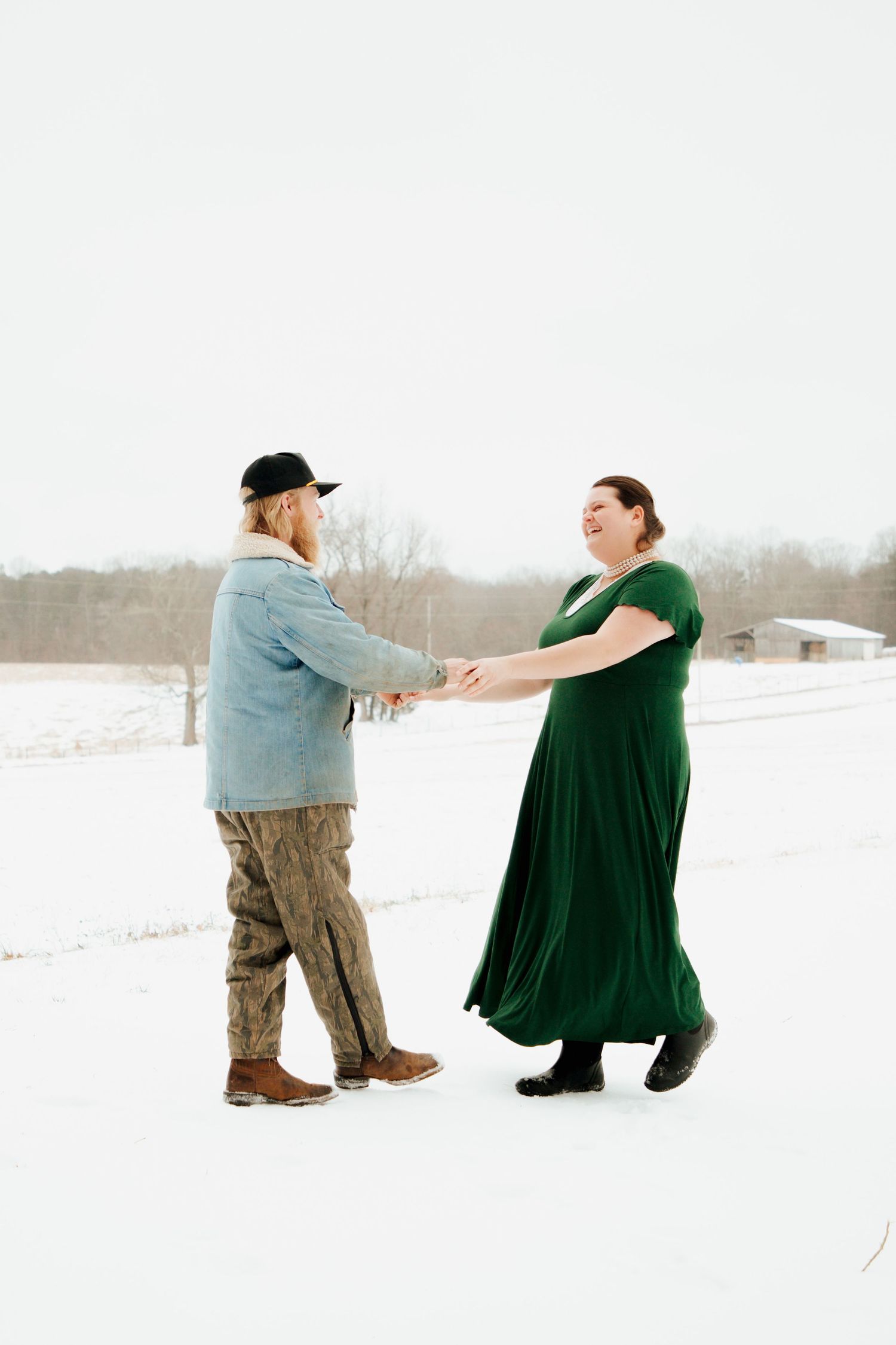 Couple holding hands and dancing outdoors in a snowy winter landscape, woman in emerald dress.