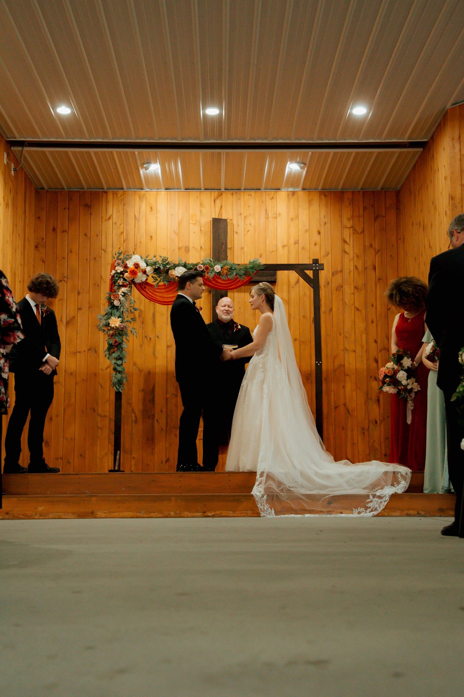 Bride and groom exchange vows at rustic wooden chapel altar decorated with floral arch and cross.