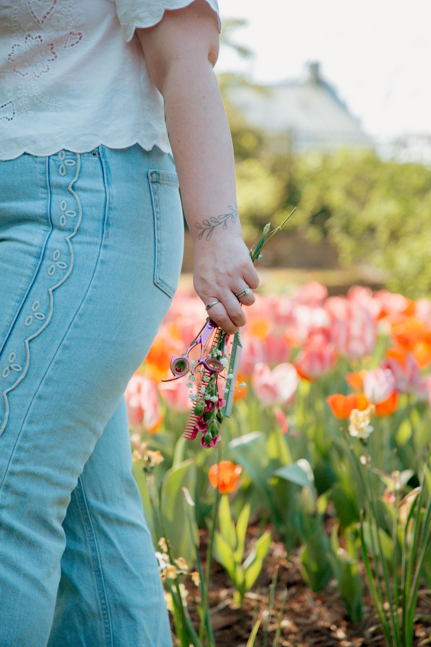 Close-up of woman's hand holding small floral bouquet while walking through colorful tulip garden.