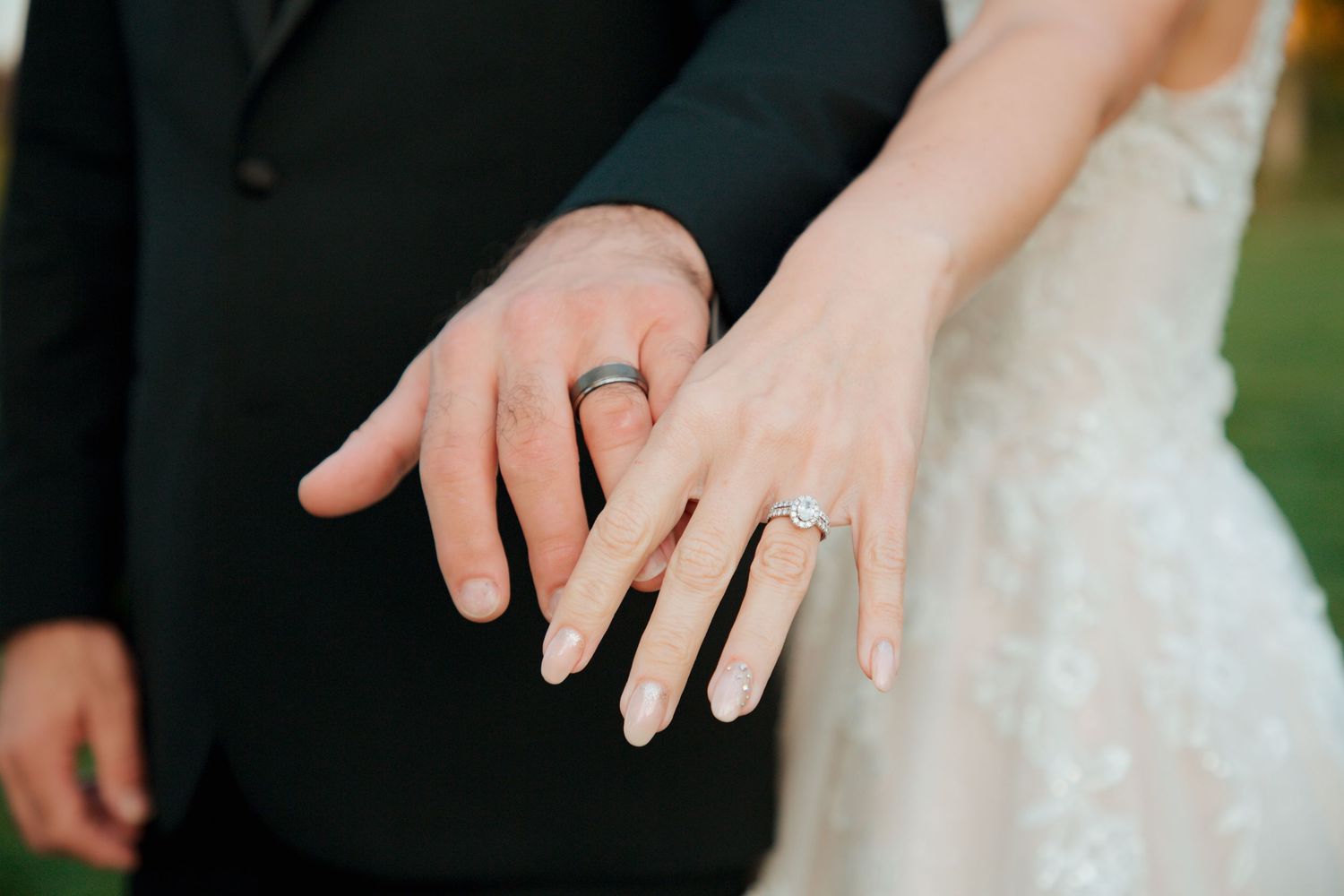 Bride and groom display wedding rings, showing diamond engagement ring and dark band.