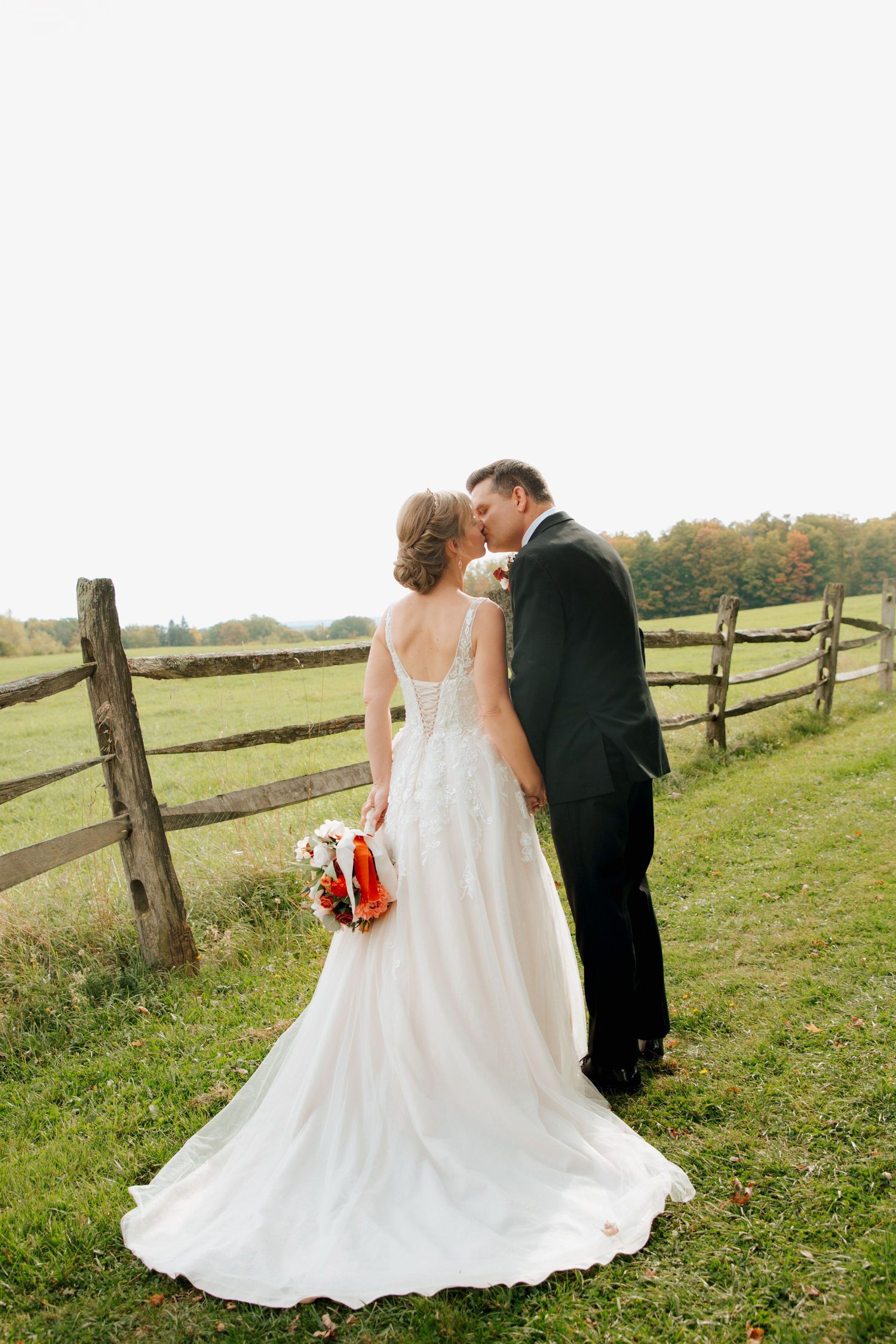 Bride and groom sharing a kiss by a rustic wooden fence in fall.