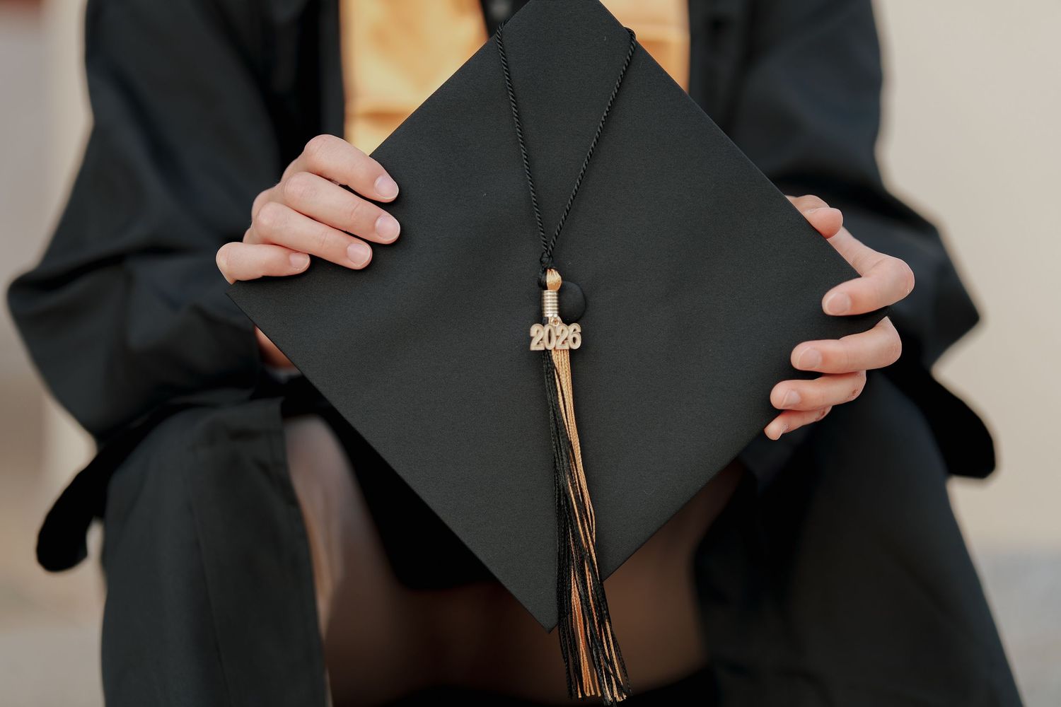Graduate holding a black mortarboard cap with a gold 2023 tassel at graduation ceremony.