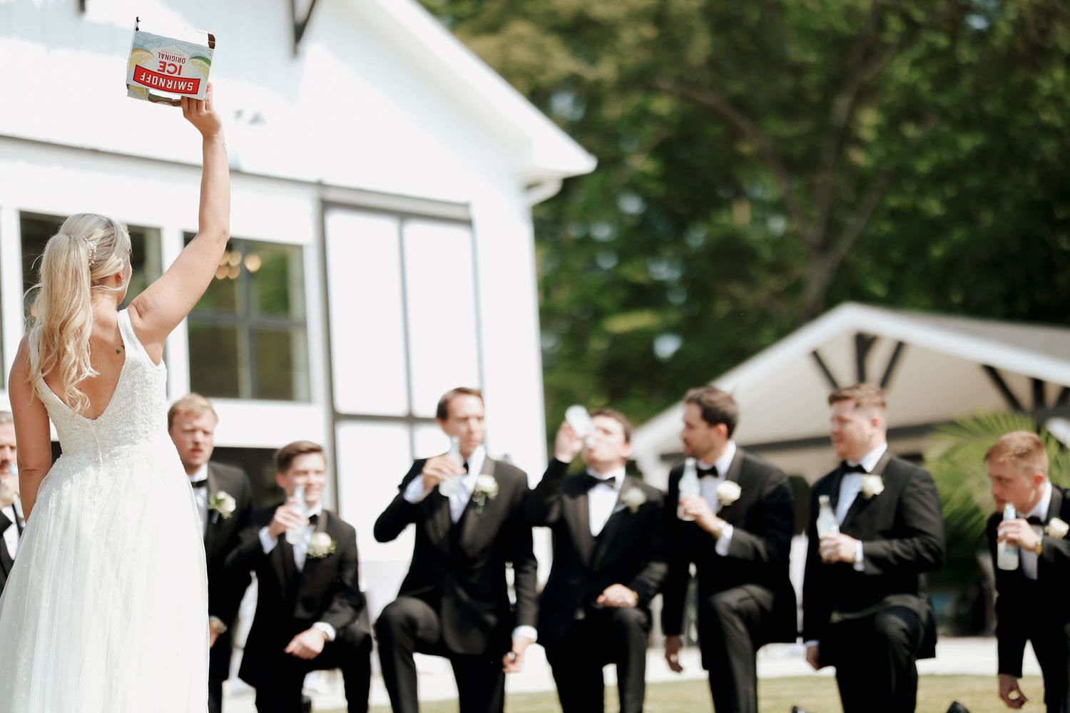 Bride holds up a box of Cheez-Its while groomsmen in black tuxedos react with excitement outdoors.