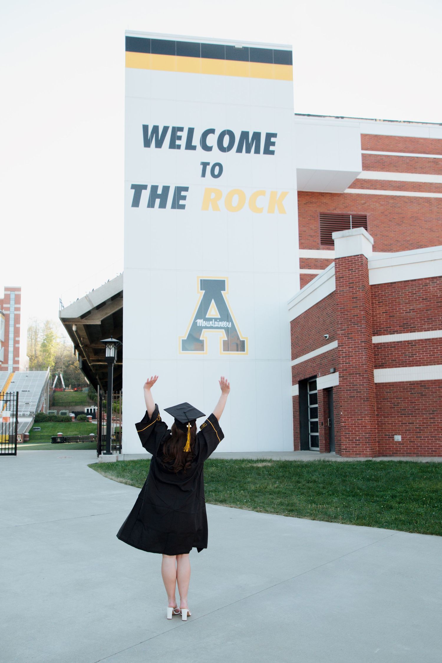 Graduate in cap and gown raising arms at Welcome to The Rock Appalachian State stadium.