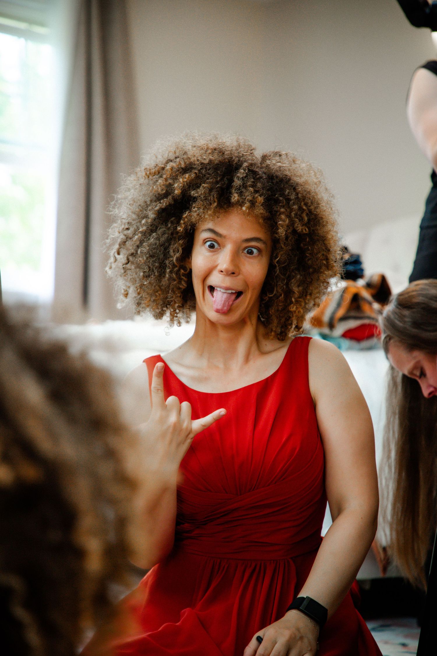 Woman in red dress making a funny face with tongue out at a wedding event.