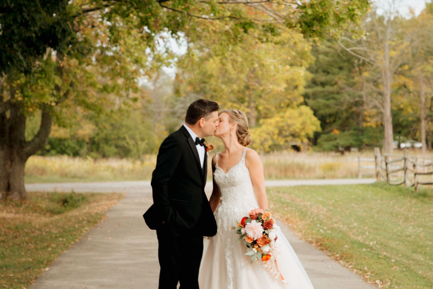 Bride and groom share a tender kiss outdoors during autumn wedding with fall foliage.