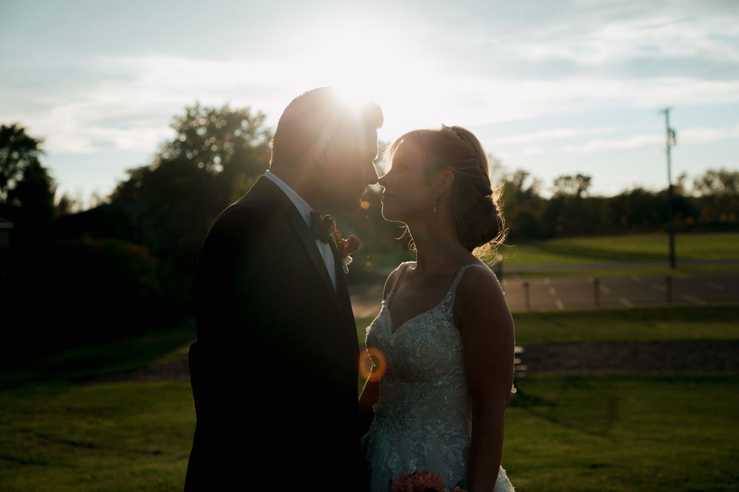 Bride and groom share a romantic silhouette moment outdoors with golden sunset backlight on their wedding day.