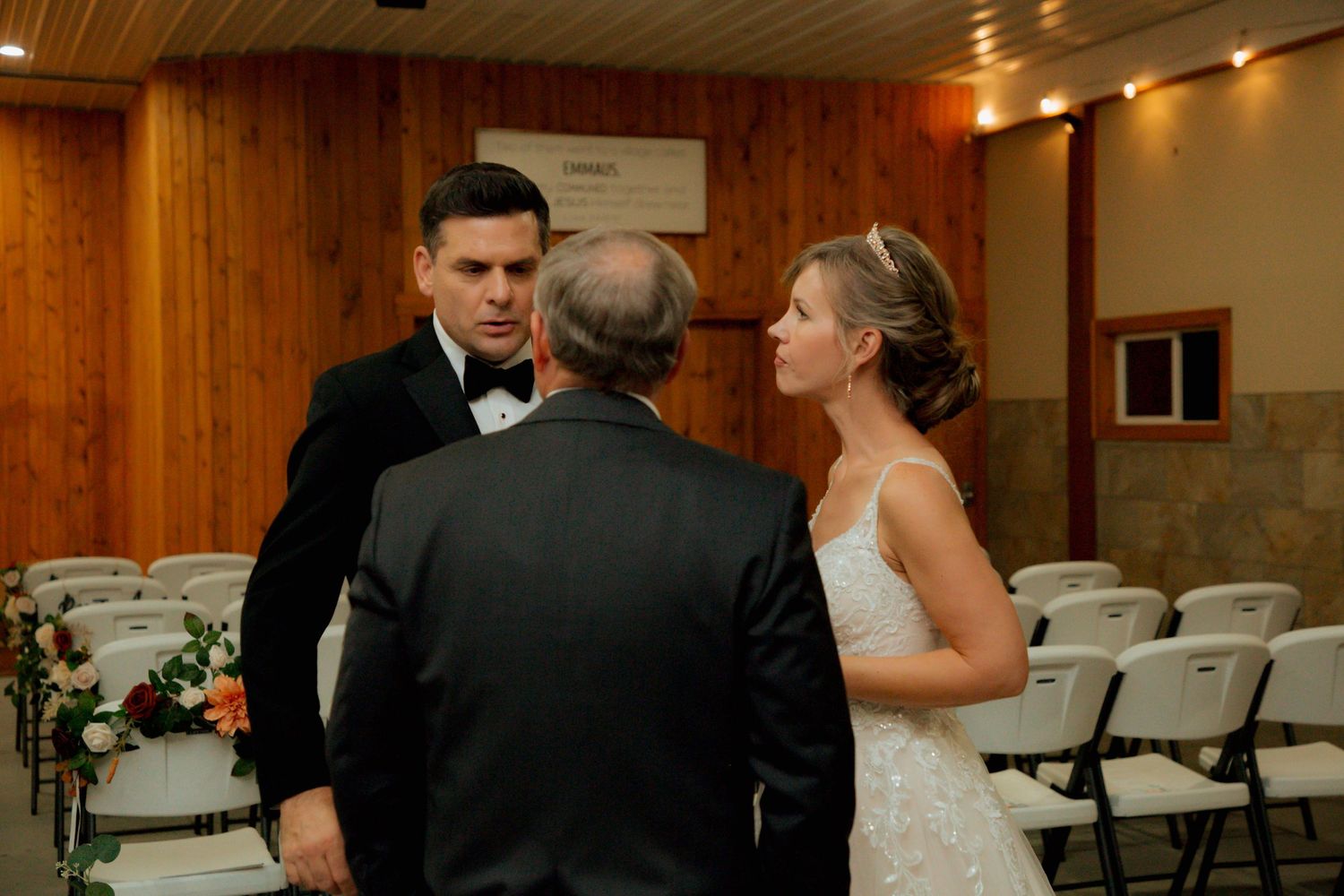 Bride and groom speak with officiant before their wedding ceremony in a wood-paneled venue.