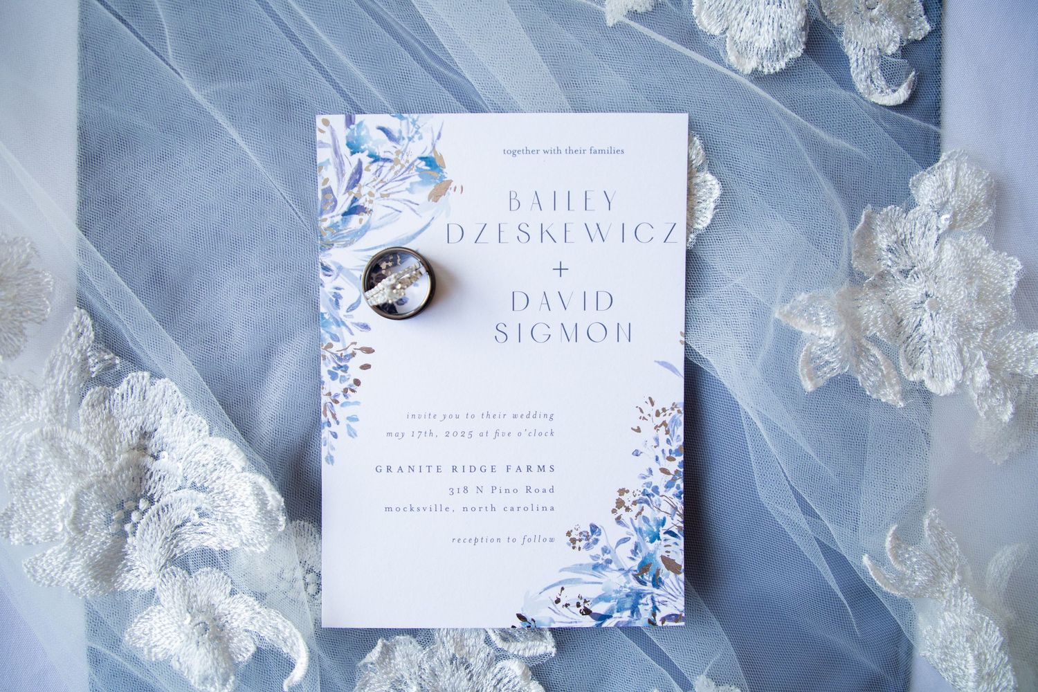 Elegant blue and white floral wedding invitation with a diamond ring resting on top.
