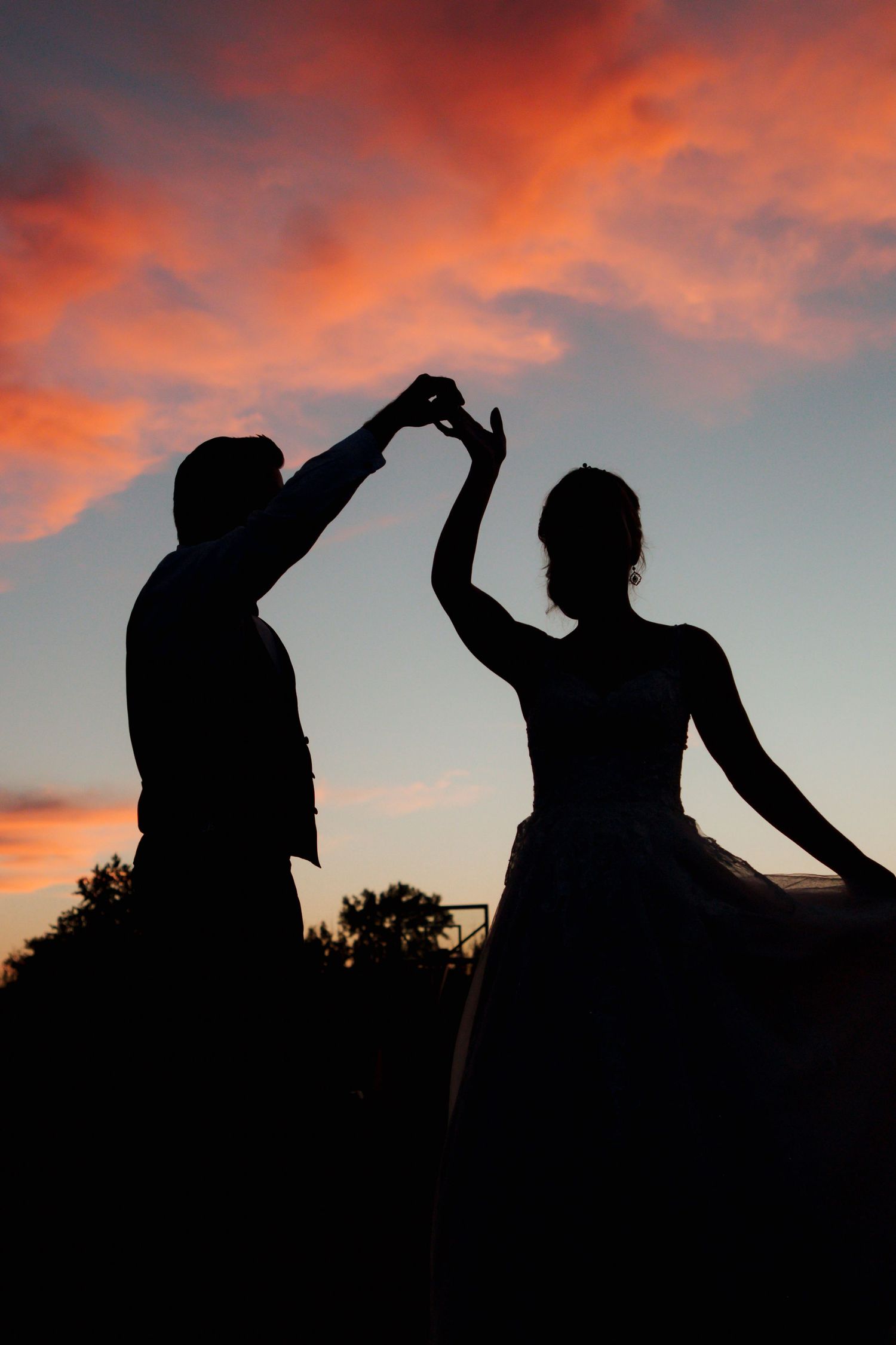 Silhouette of bride and groom dancing together under a dramatic colorful sunset sky.