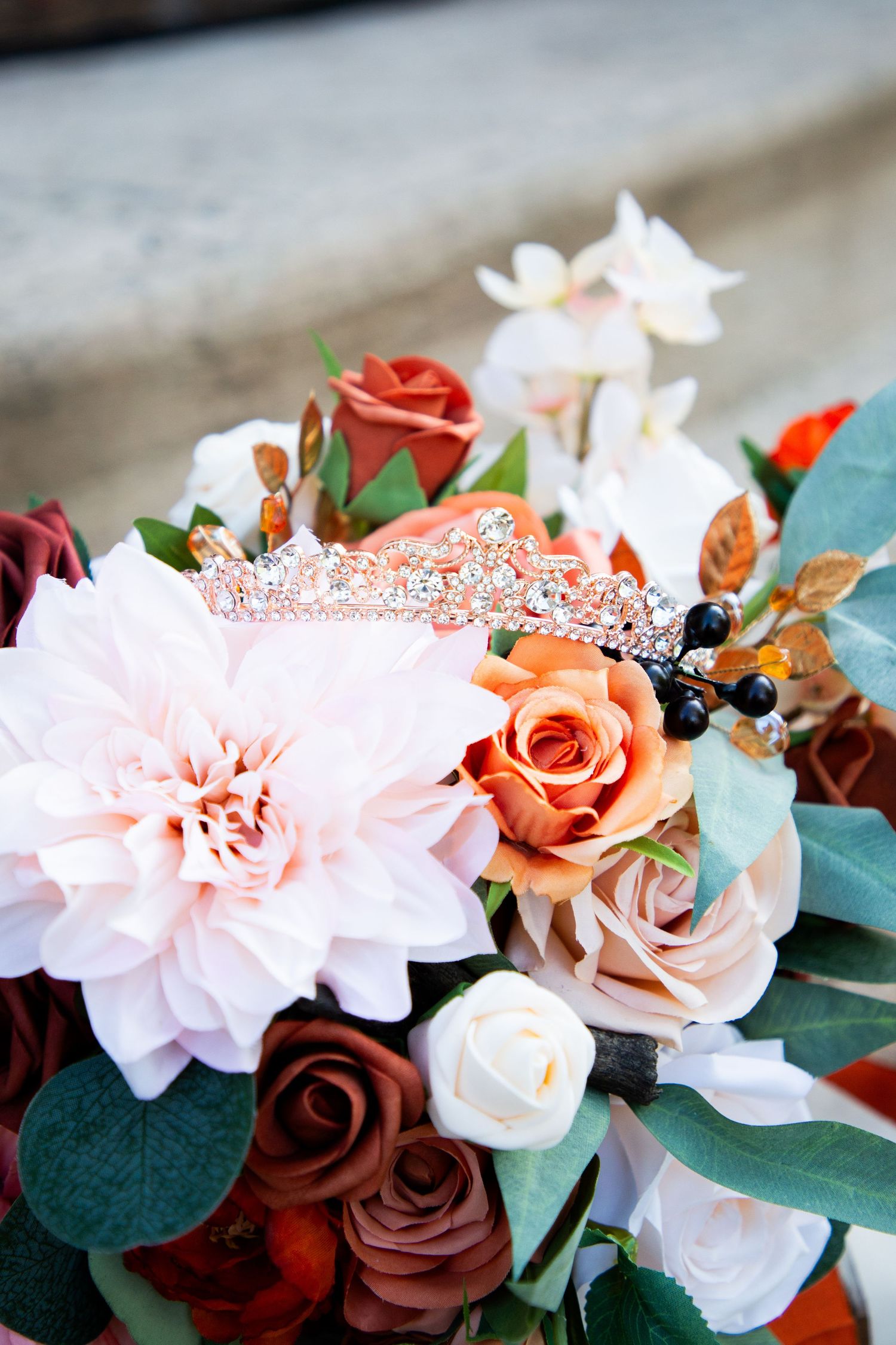 Rose gold crystal bridal tiara nestled in a bouquet of terracotta, blush, and burgundy wedding flowers.