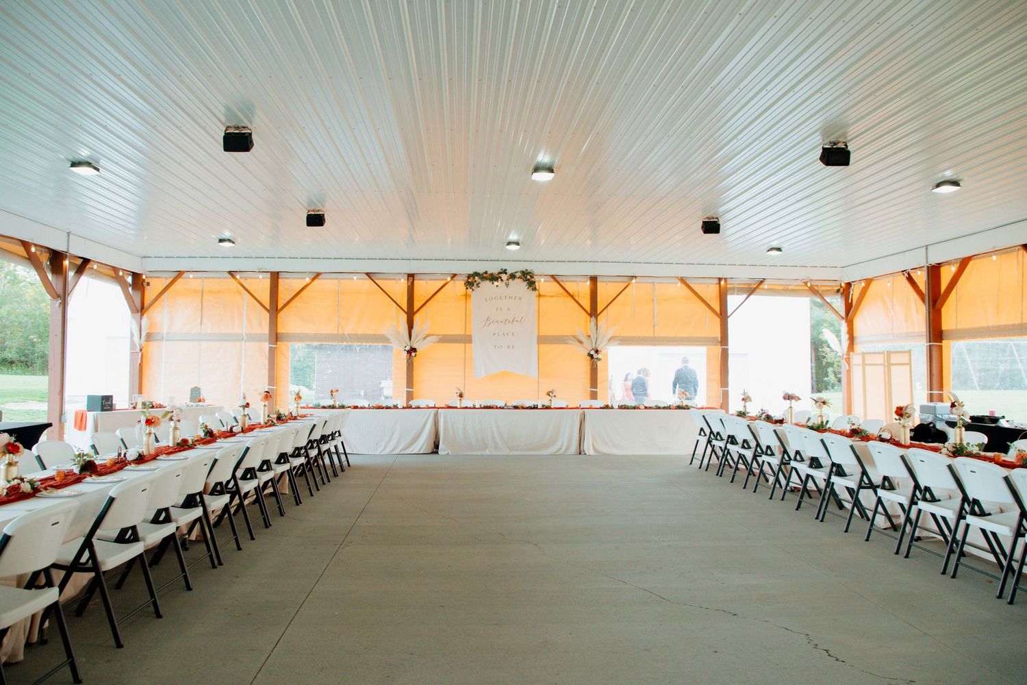 Spacious barn wedding reception venue with long guest tables and white folding chairs.