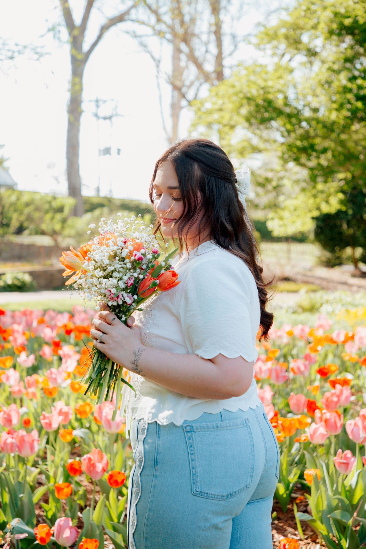 Woman smells colorful bouquet of orange tulips and white flowers while standing in tulip garden.
