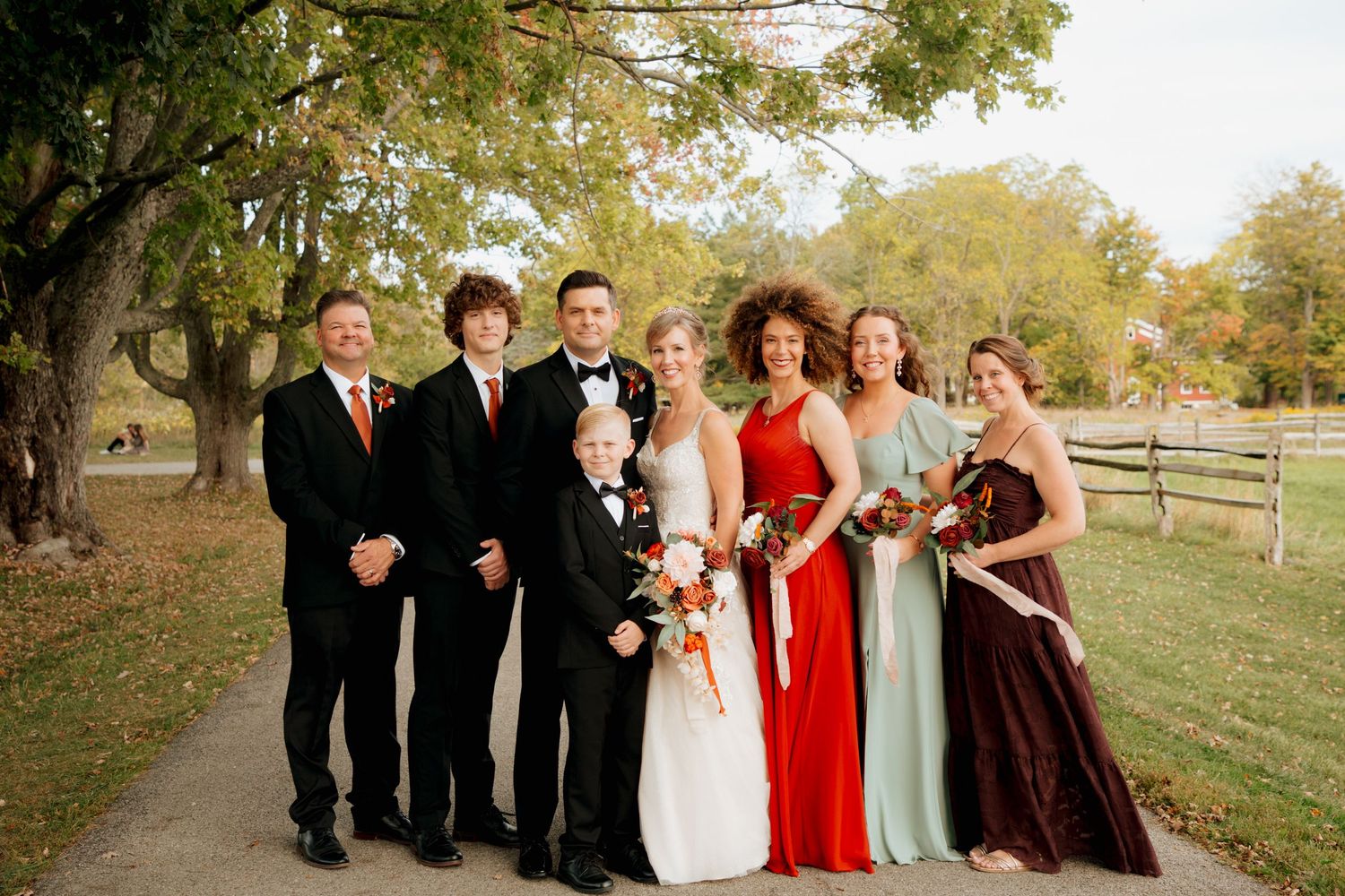 Bride and groom with wedding party in autumn colors on outdoor path.