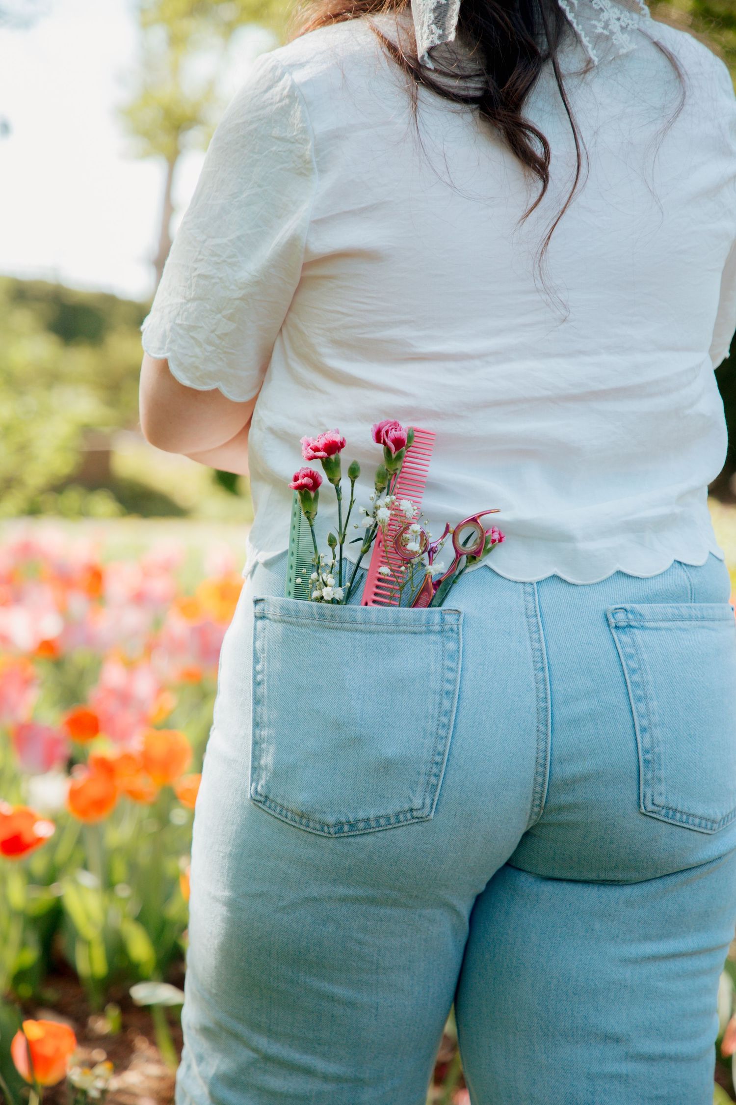 Back view of woman in light blue jeans with pink flowers and comb tucked in back pocket near tulip field.