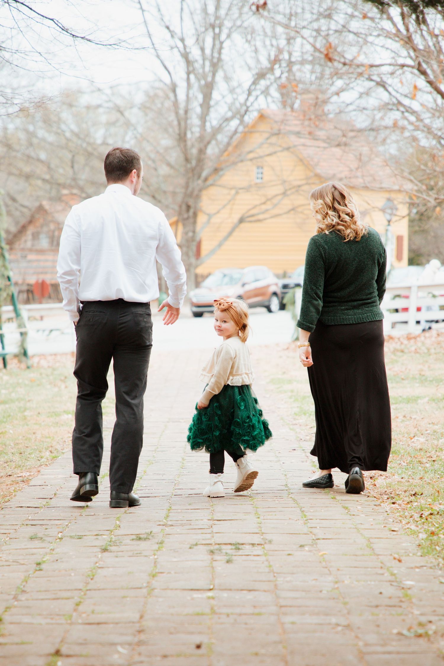 Family of three walking away on brick path during outdoor fall family photo session.
